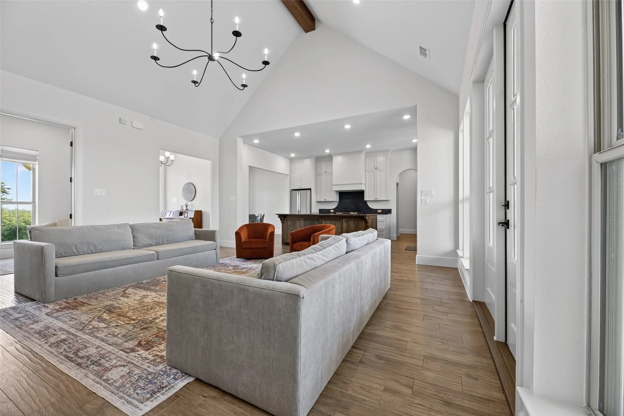 Vaulted ceilings, exposed wood beam accent, wood-finish flooring, recessed lighting, and a modern chandelier