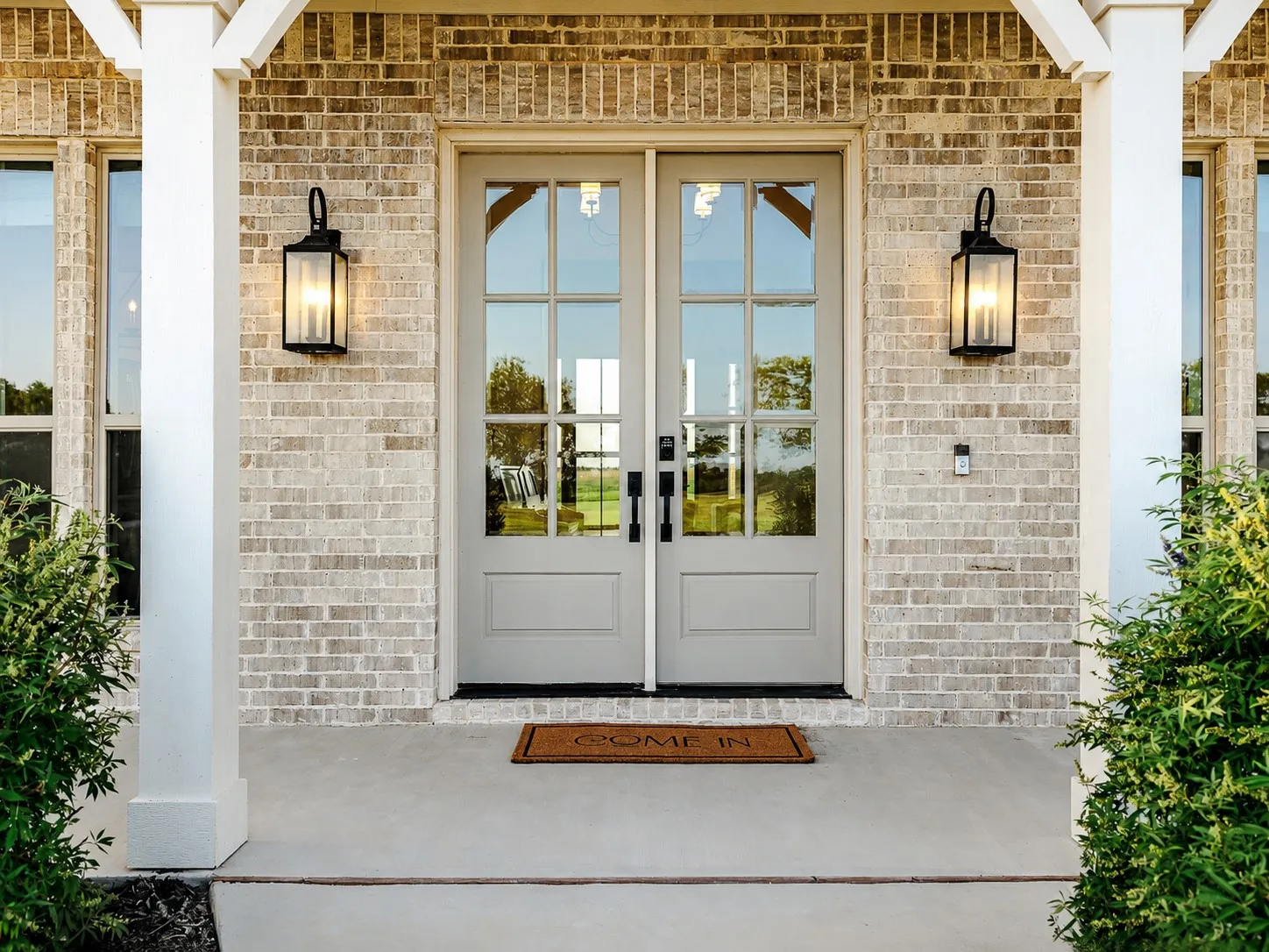 Welcoming entry featuring dual French doors with multiple glass panes, flanked by symmetrical black lantern sconces and white structural columns