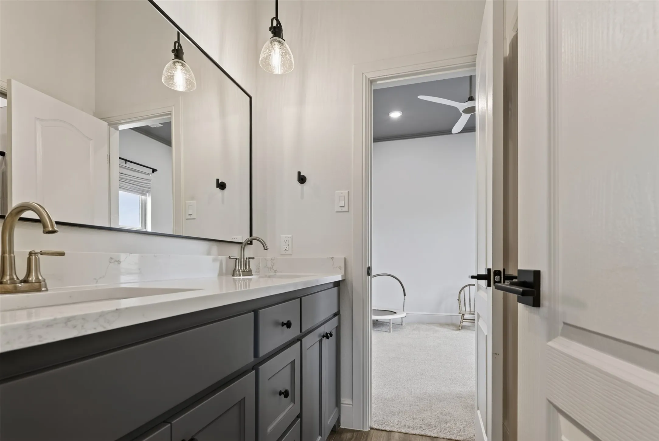 Primary bathroom featuring a dark-finished vanity with dual sinks, white quartz countertop, brass-finish faucets, and a large framed mirror