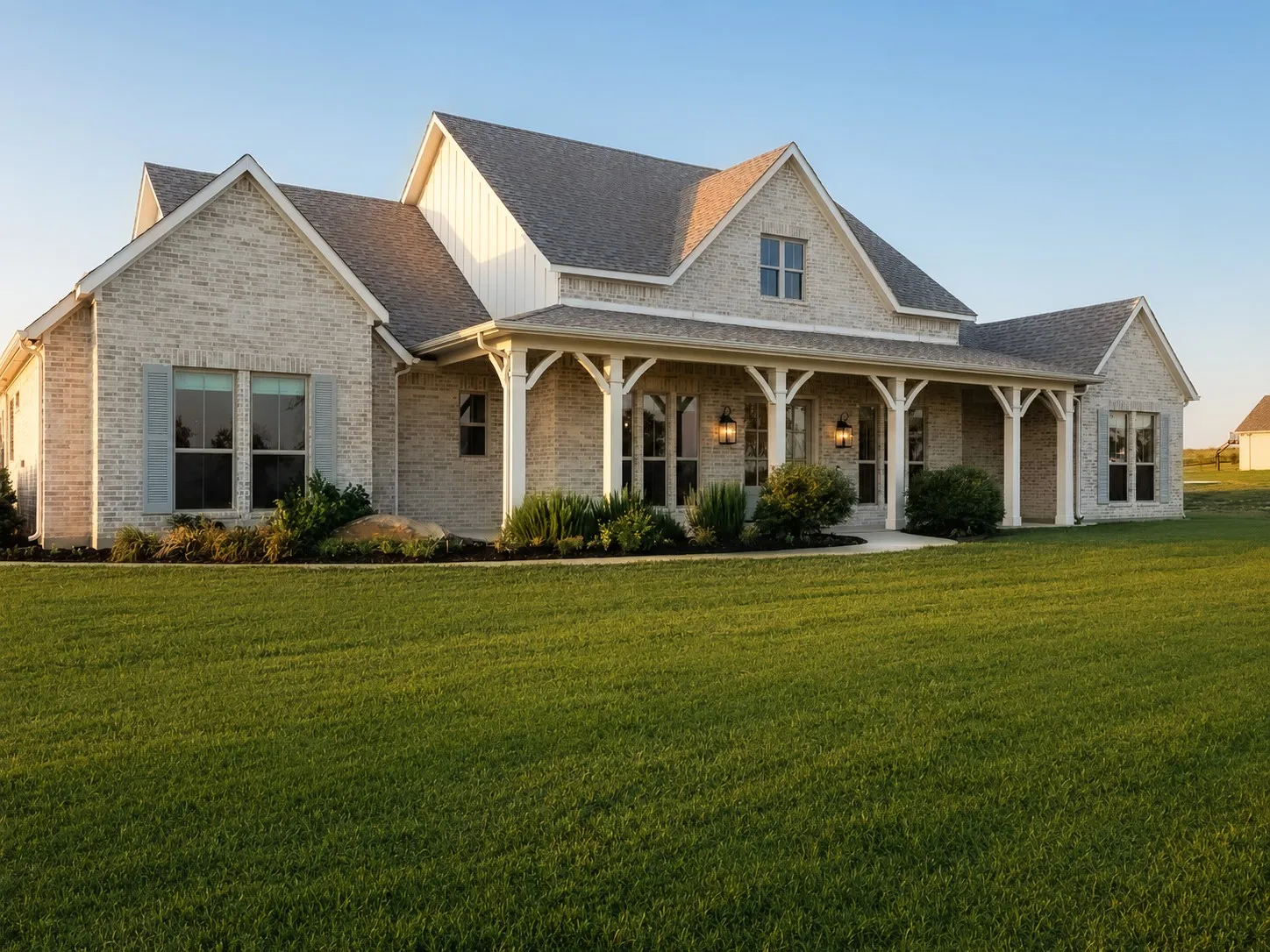 Elegant brick and stone farmhouse with a welcoming covered front porch featuring classic columns and wood-finish detailing