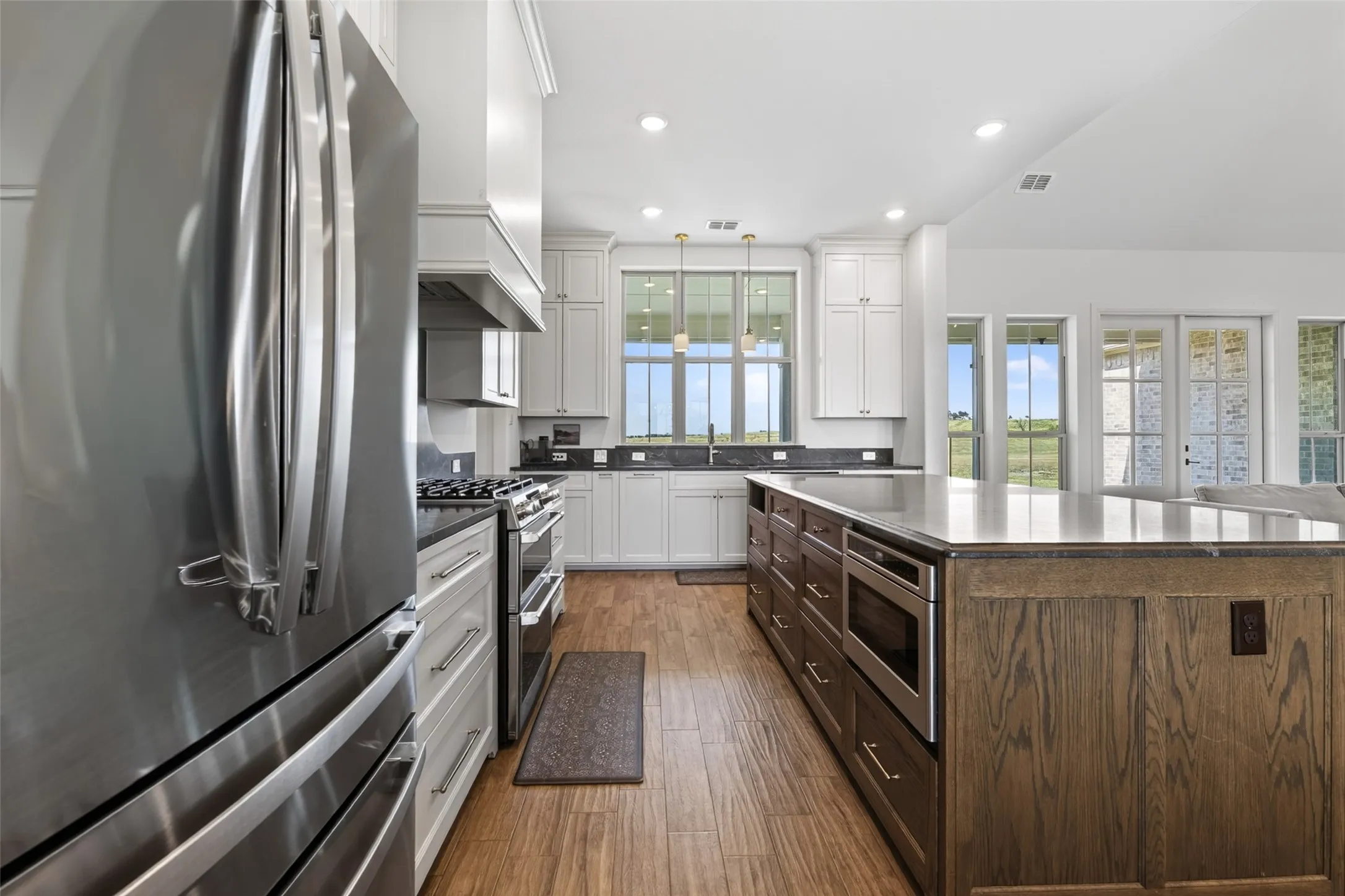 Stainless steel appliances, white cabinetry, wood-finish flooring, a kitchen island with built-in microwave, and recessed lighting