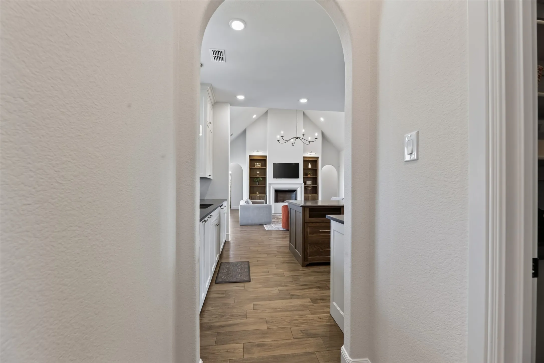 Archway entry to an open-concept interior with vaulted ceilings, recessed lighting, wood-finish flooring, and a central island