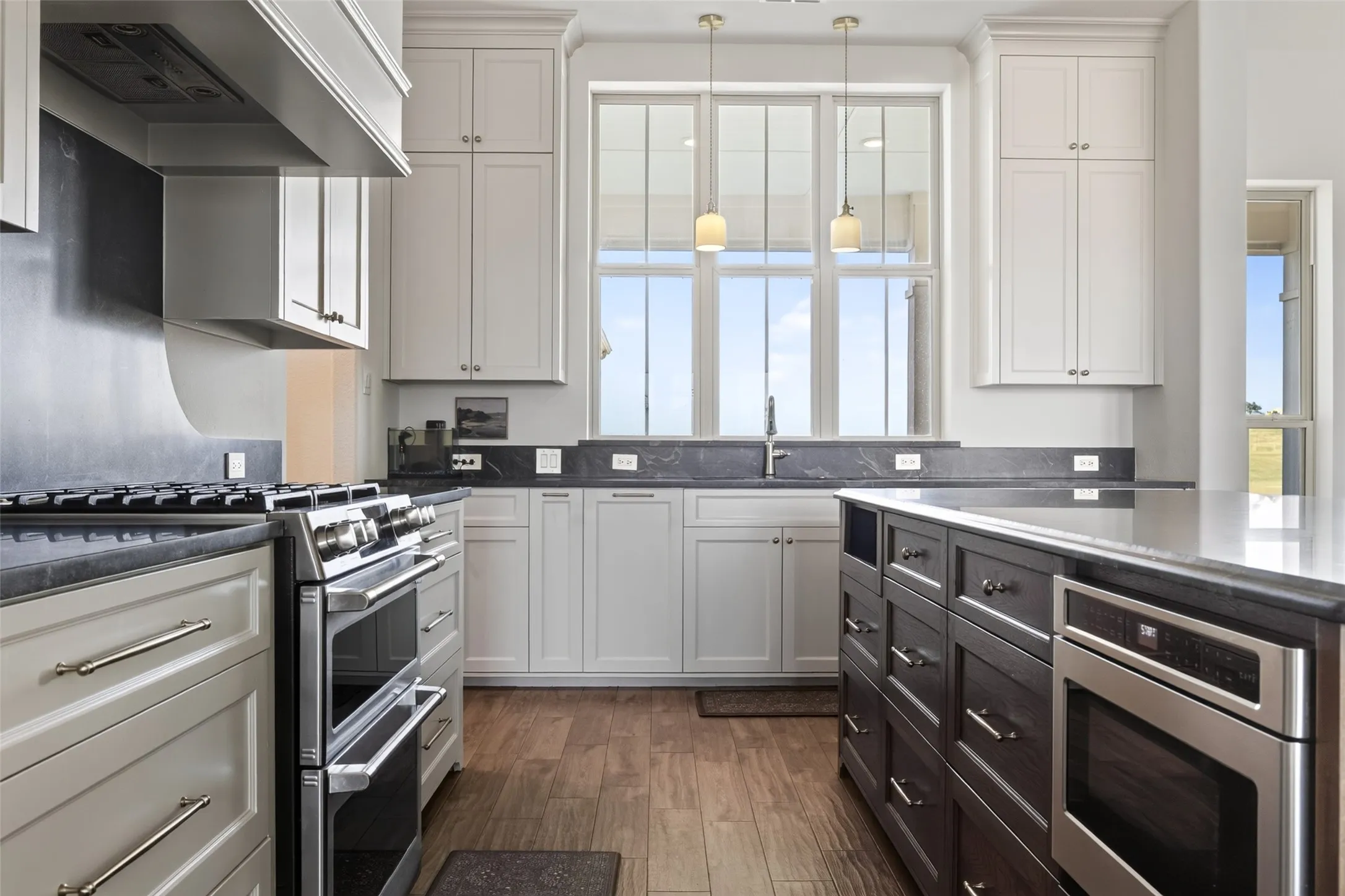 Kitchen featuring a large window, pendant lighting, wood-finish flooring, a stainless steel double oven range, and a built-in stainless steel oven