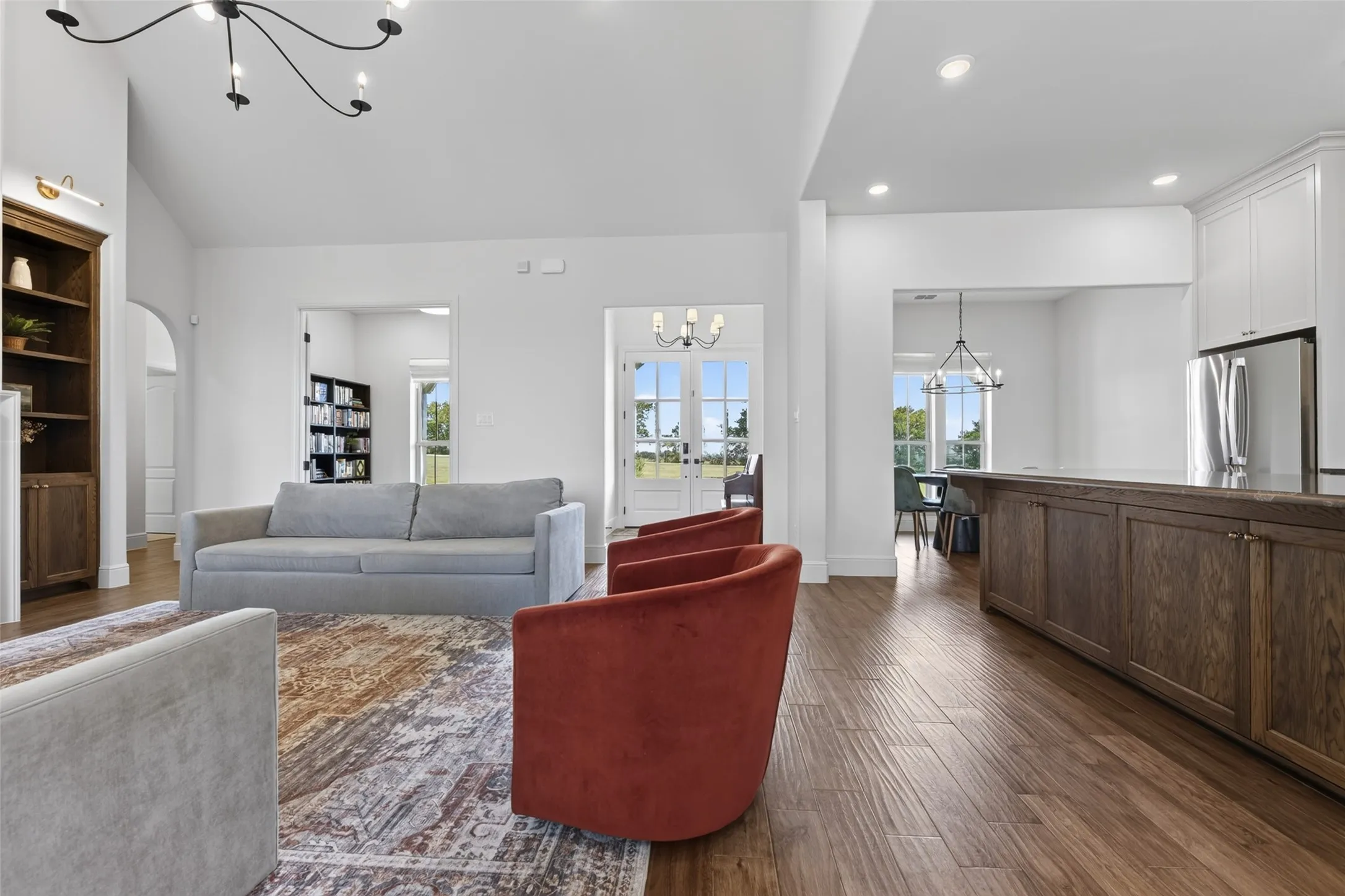 Vaulted ceiling with a contemporary chandelier, recessed lighting, wood-finish flooring, built-in wooden shelving, and a kitchen island with wood-finish cabinetry