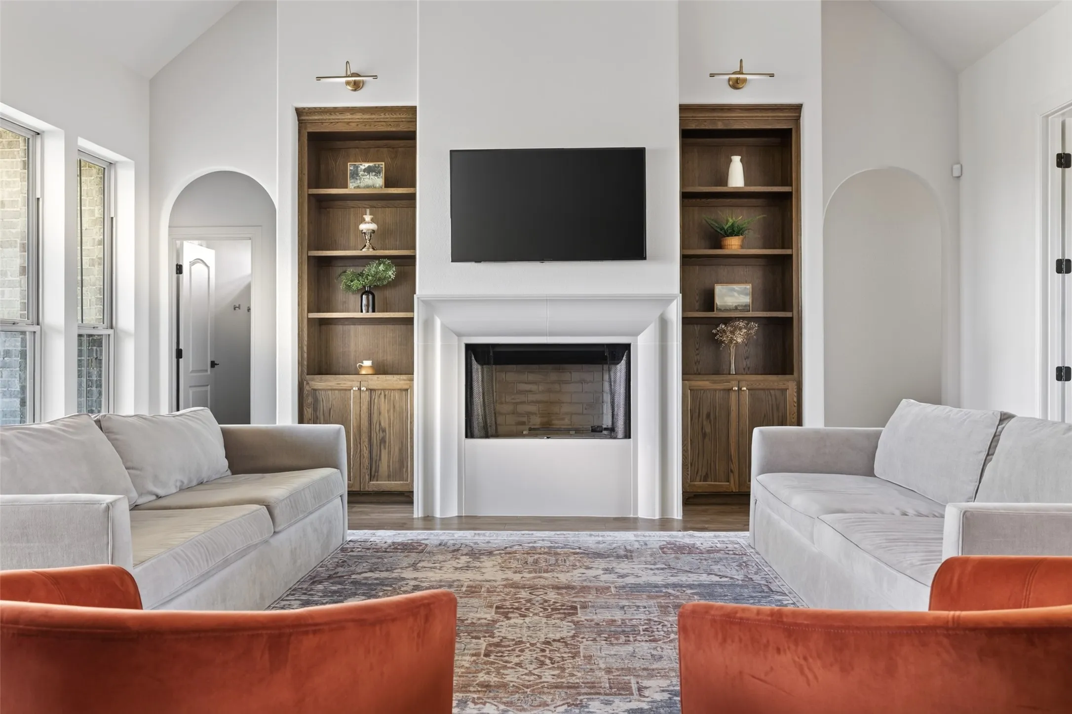 Vaulted ceiling, built-in shelving, fireplace with mantel, arched doorways, and wood-finish flooring