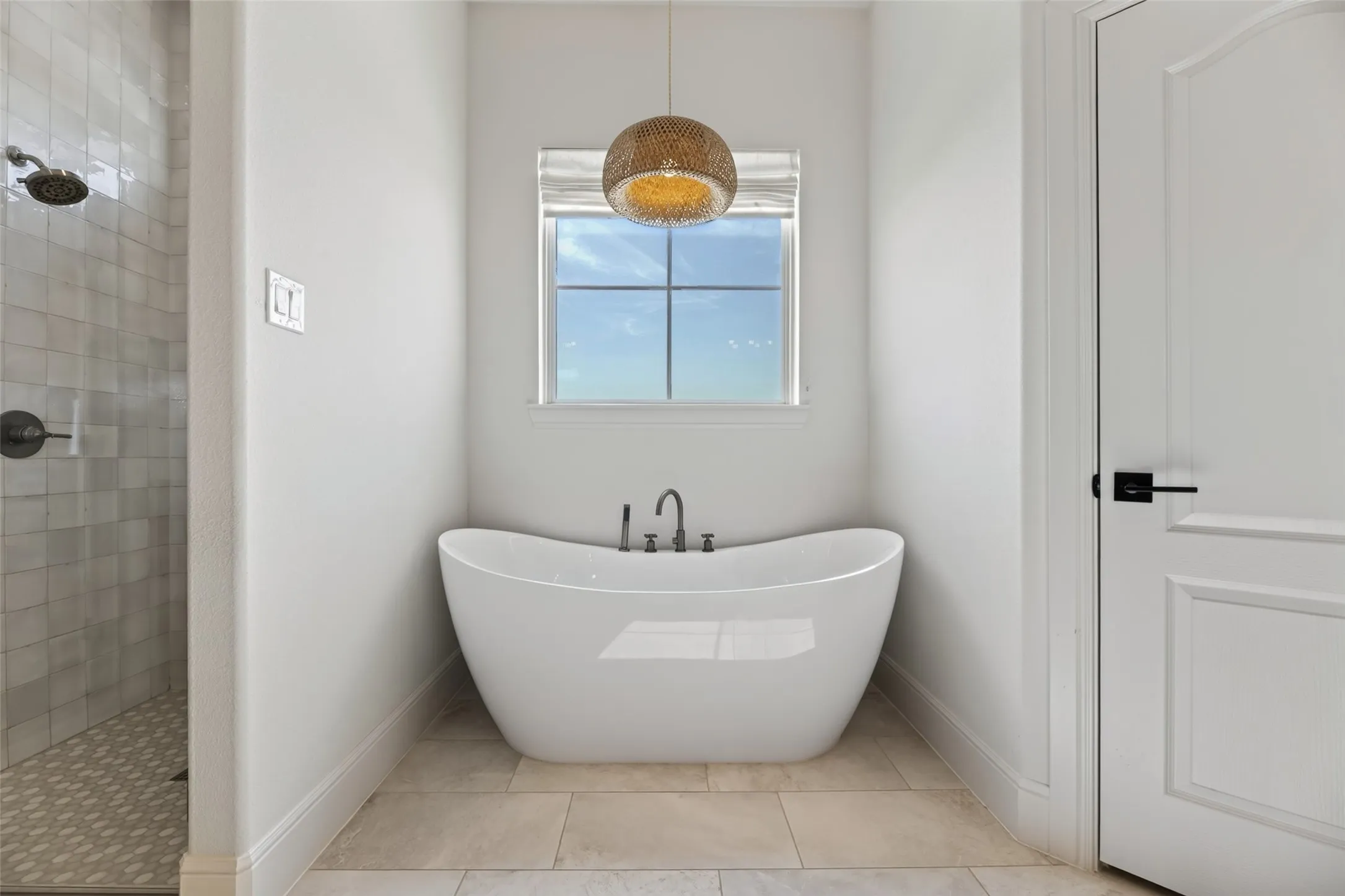 Freestanding soaking tub with dark-toned fixtures and a decorative overhead light fixture