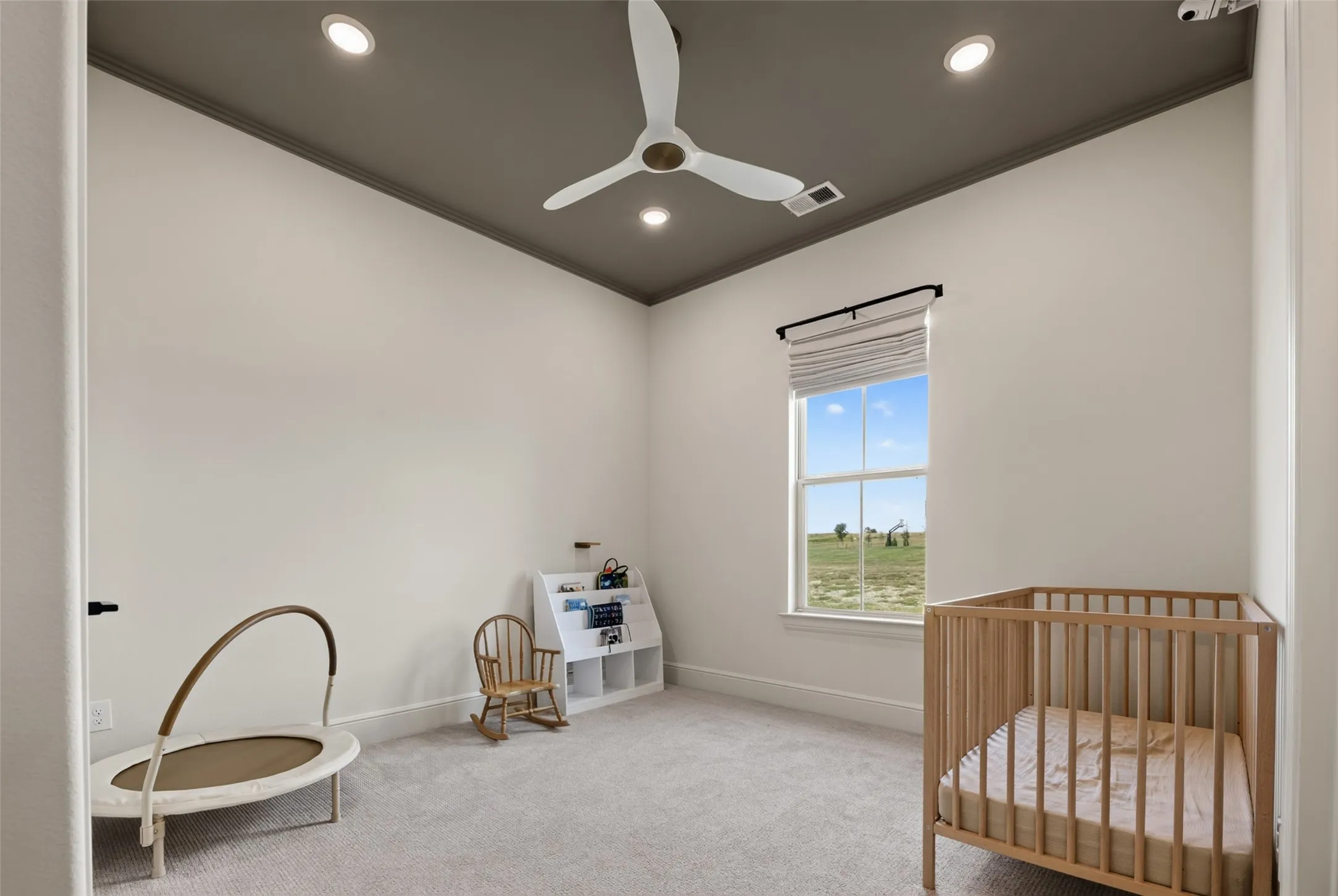 Bright nursery featuring recessed lighting, a ceiling fan with pull-chain operation, large window with natural light exposure, wood-finish crib, and neutral carpet flooring throughout