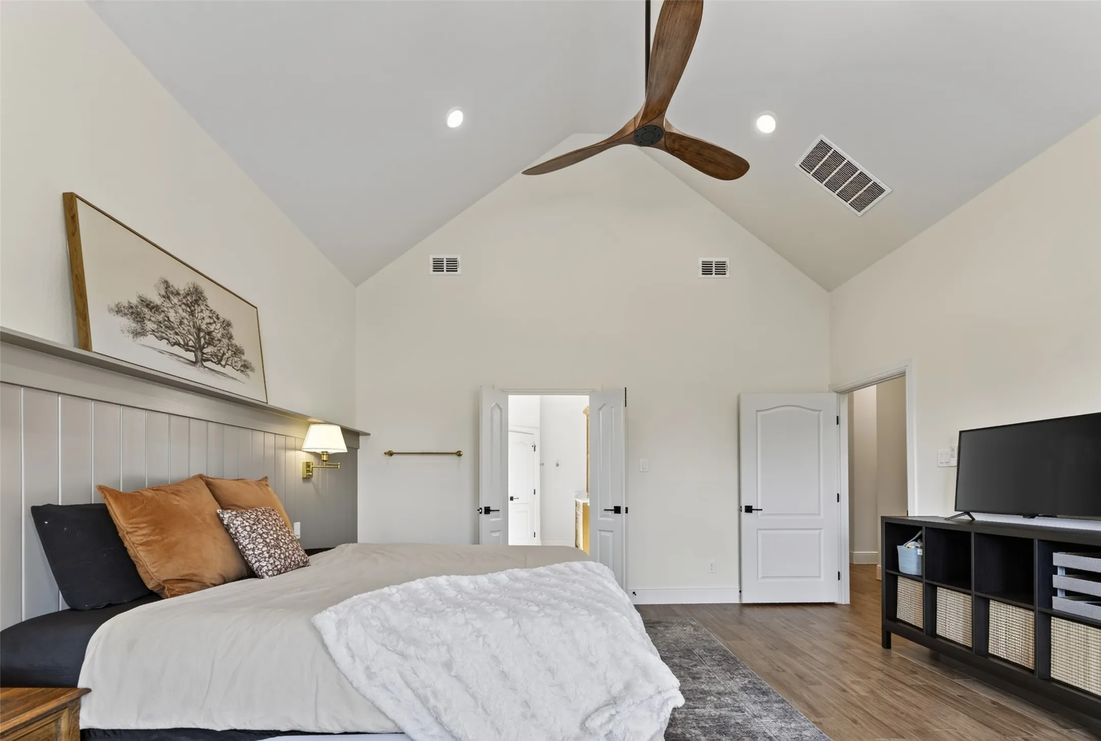 Primary bedroom suite featuring vaulted ceilings with exposed wood beam and recessed lighting, wood-finish flooring throughout, and an ensuite bathroom