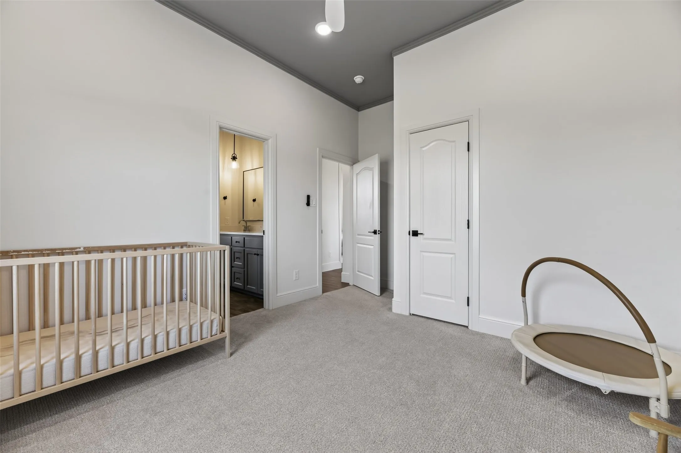 Carpeted room featuring a white interior door with black hardware, vaulted ceiling with grey paint, and an en-suite bathroom with a dark vanity and wall-mounted light fixture