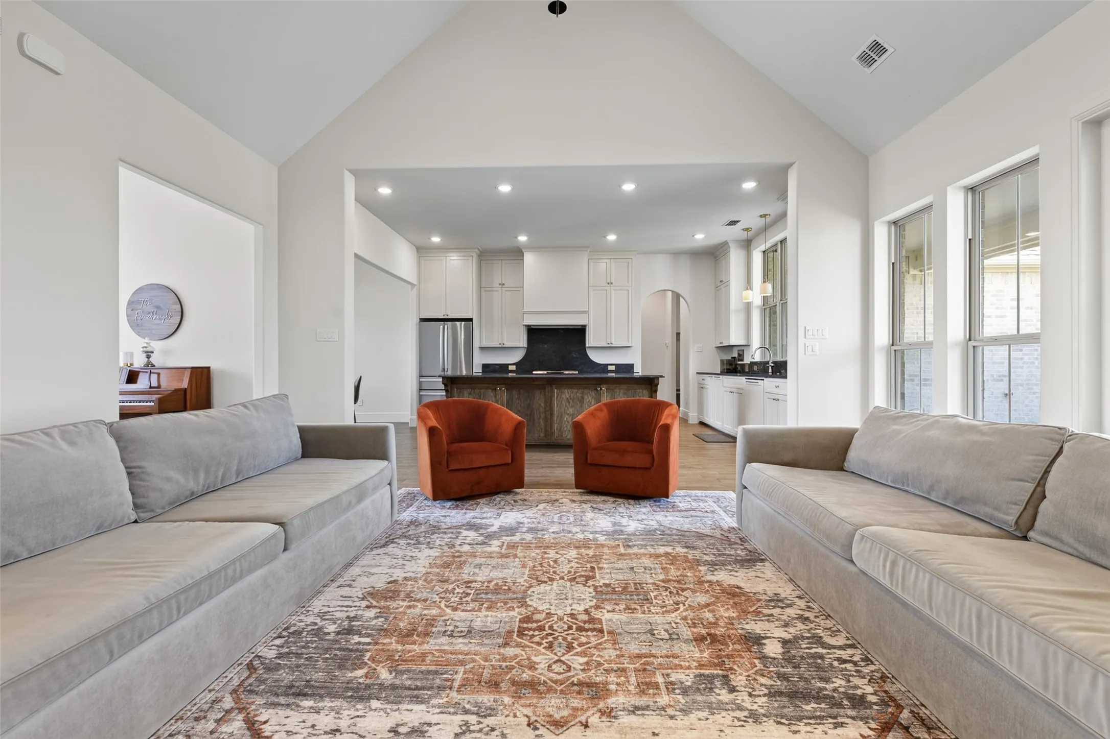 Vaulted ceiling with recessed lighting, wood-finish flooring, white cabinetry, dark countertop, and stainless steel appliances