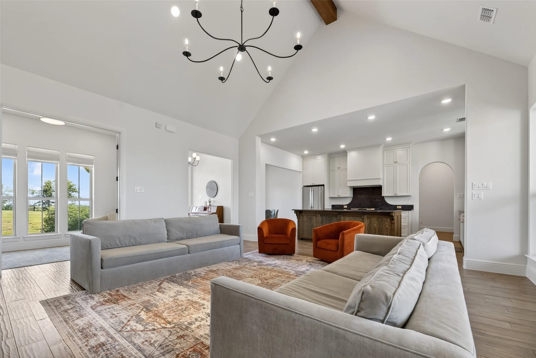 Open-concept living space featuring soaring vaulted ceilings with recessed lighting and a modern spiked chandelier, wide-plank wood-finish flooring throughout, and multiple seating areas anchored by a geometric area rug