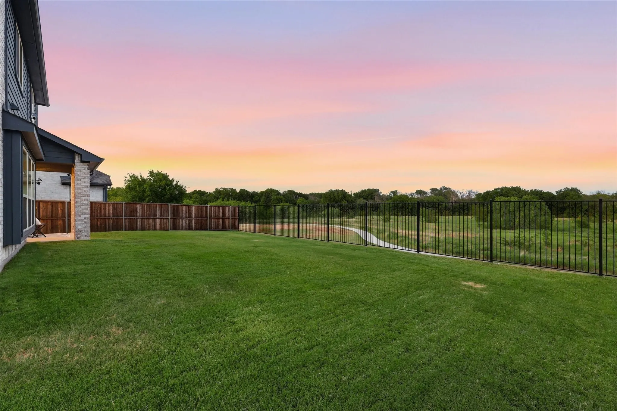 Expansive back lawn featuring a covered rear patio with privacy fencing and wrought iron fencing overlooking the greenbelt.