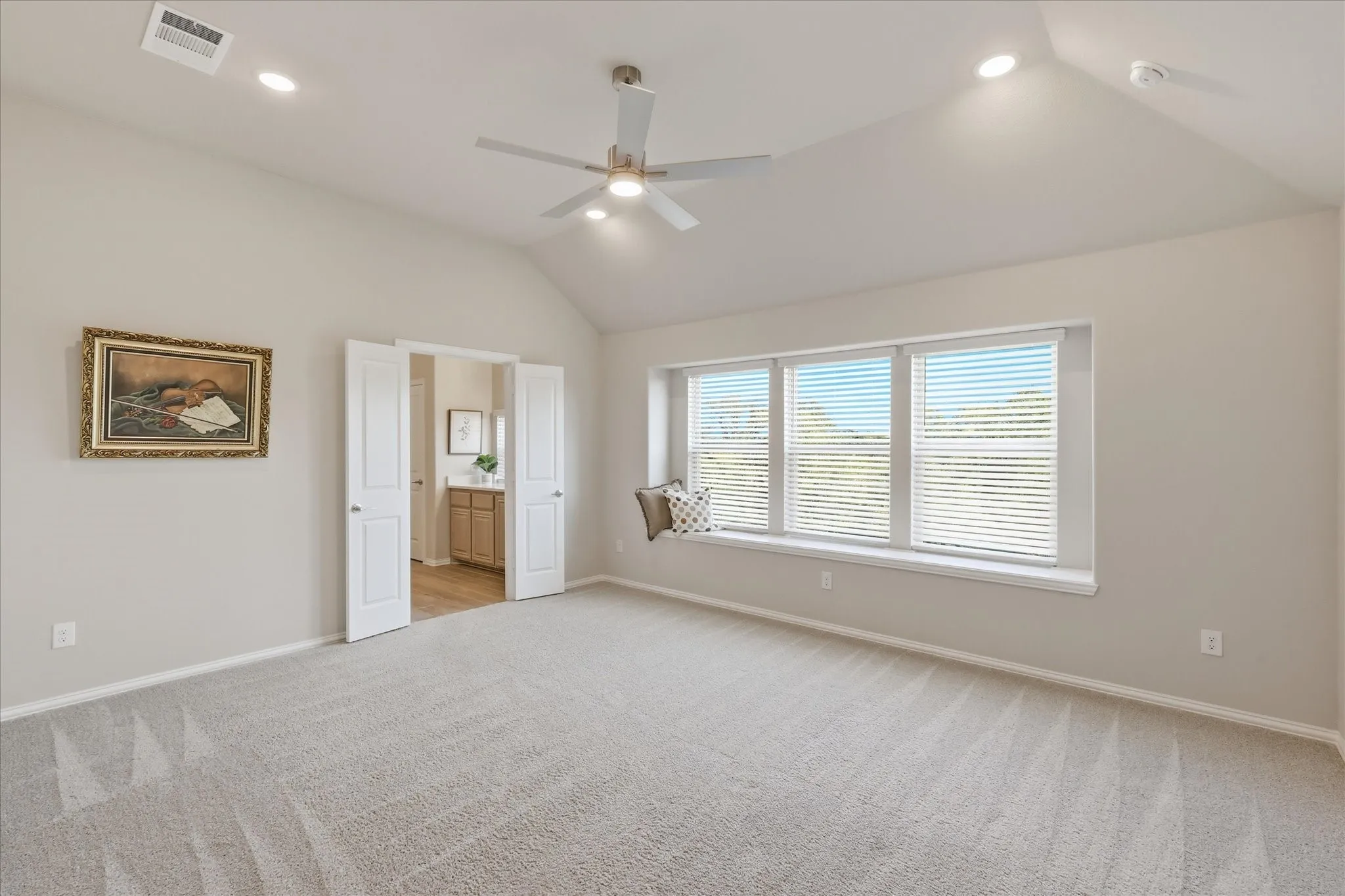 Second floor primary bedroom, featuring vaulted ceiling with recessed lighting and ceiling fan, bay window seating, ensuite bathroom