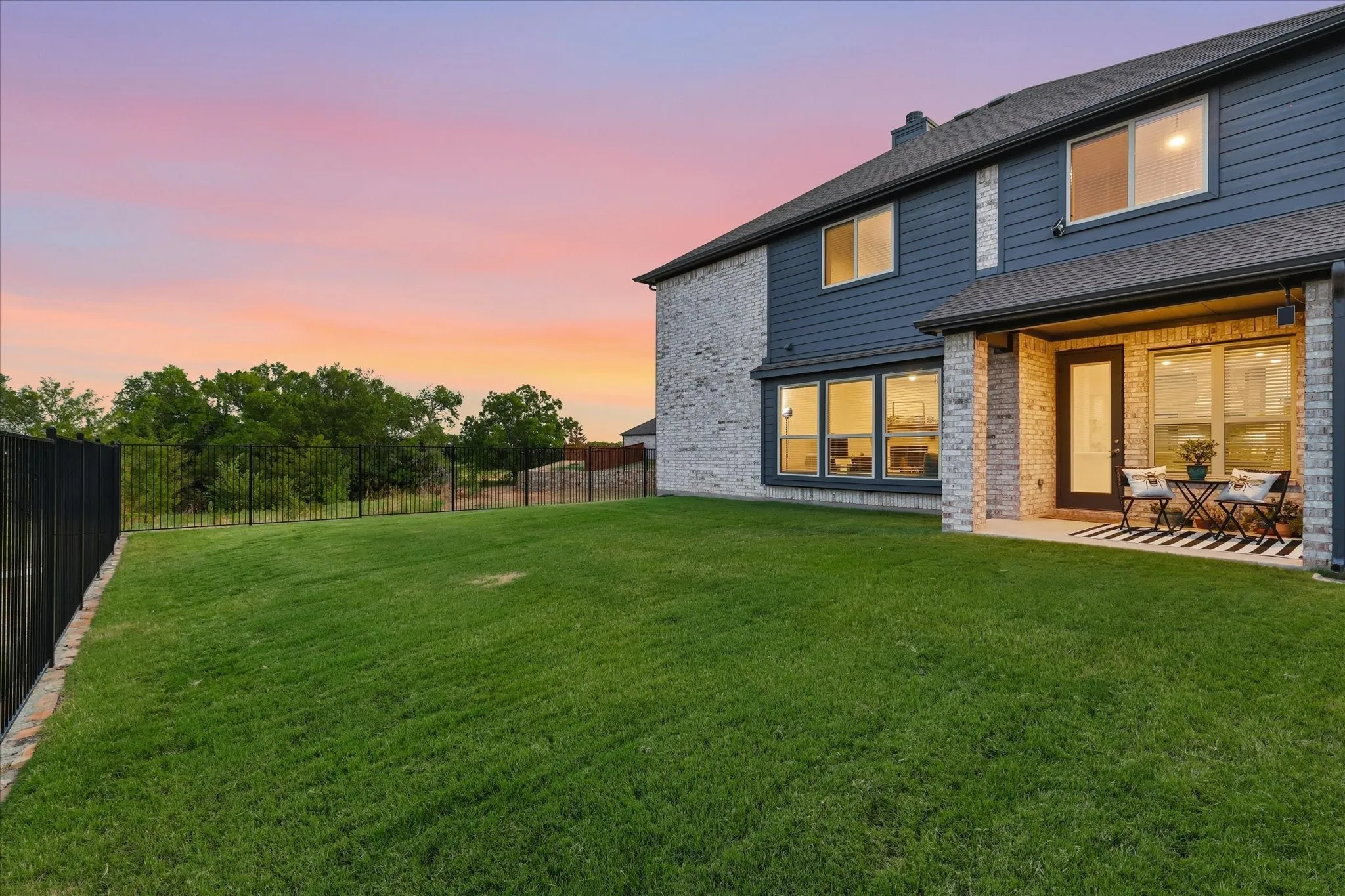 Expansive back lawn featuring a covered rear patio with privacy fencing and wrought iron fencing overlooking the greenbelt.
