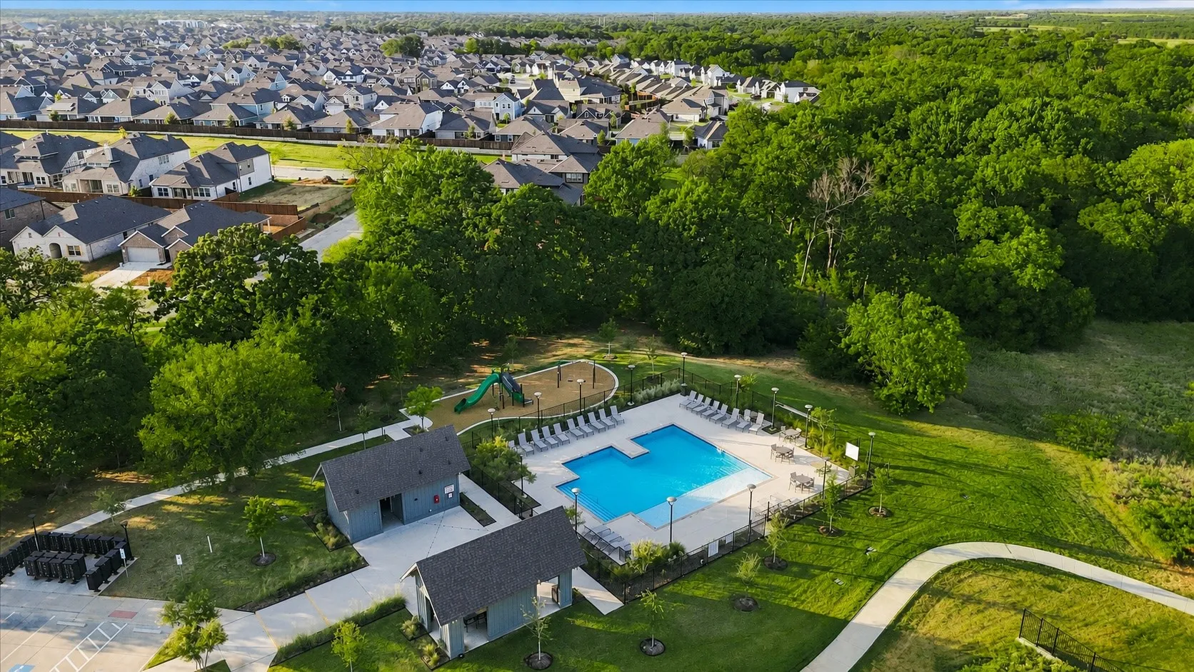 Community amenities featuring a swimming pool, shaded lounge area, playground, and green space, surrounded by mature trees