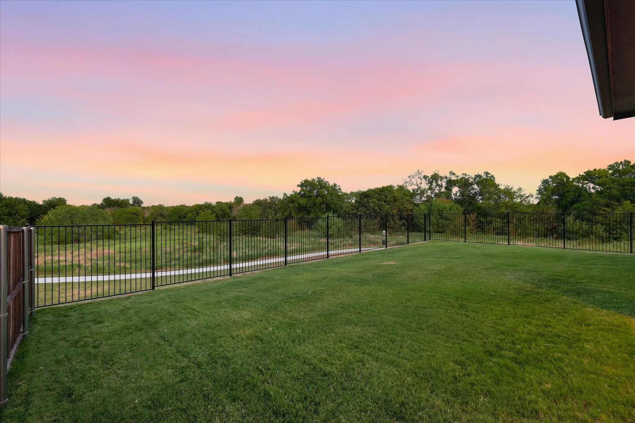 Expansive back lawn featuring a covered rear patio with privacy fencing and wrought iron fencing overlooking the greenbelt.