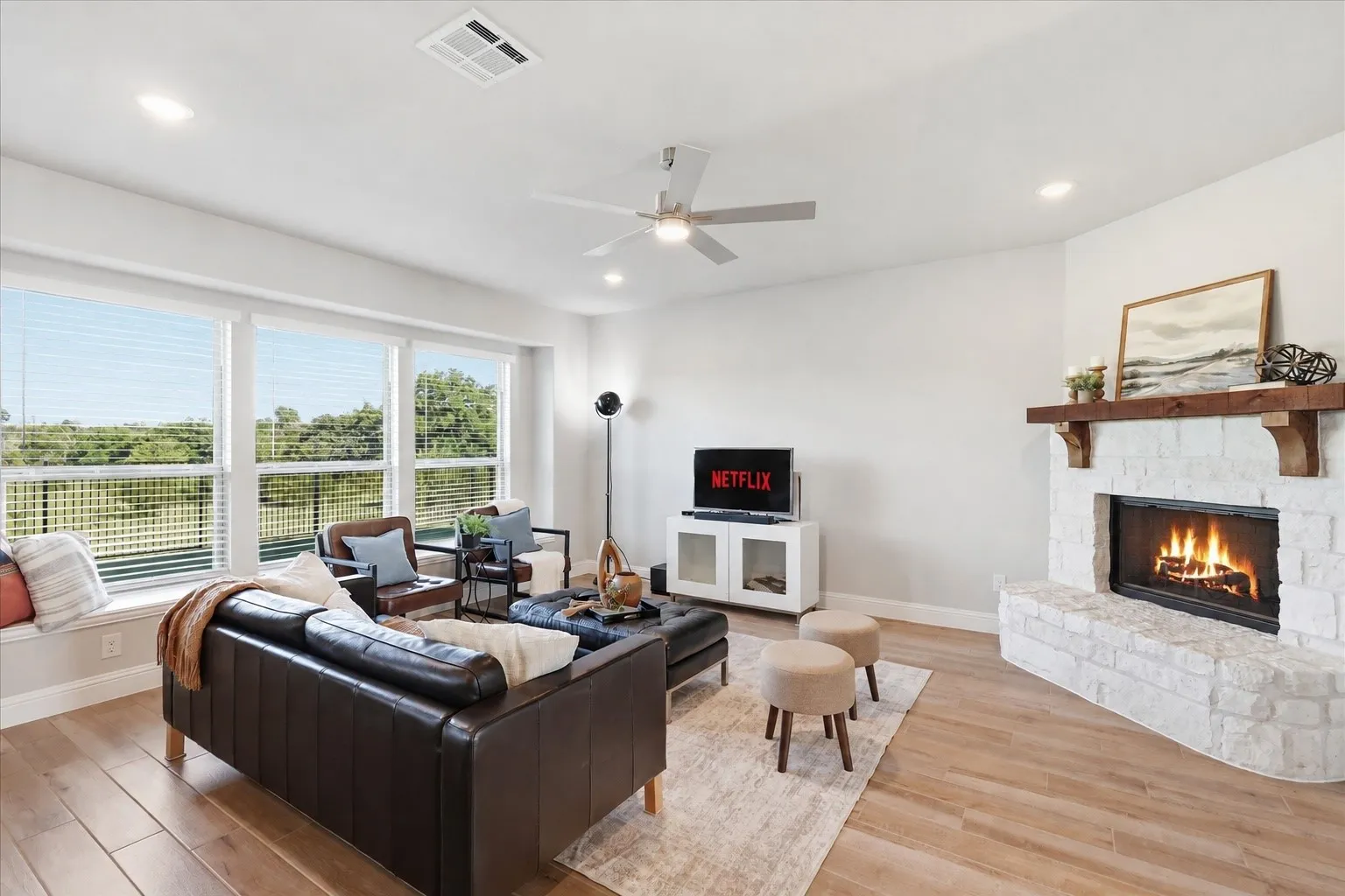 Spacious living area featuring a stone fireplace with a wood mantel, wood-finish flooring, recessed lighting, and a ceiling fan