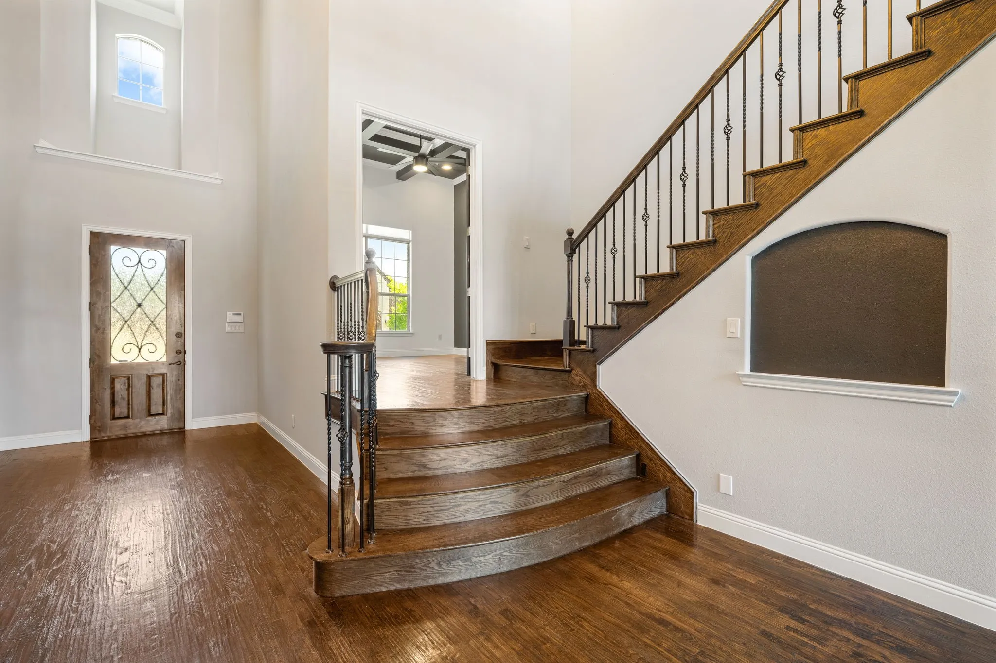 Grand foyer showcasing a curved wooden staircase with metal railings, wide-plank wood-finish flooring throughout, and soaring ceilings