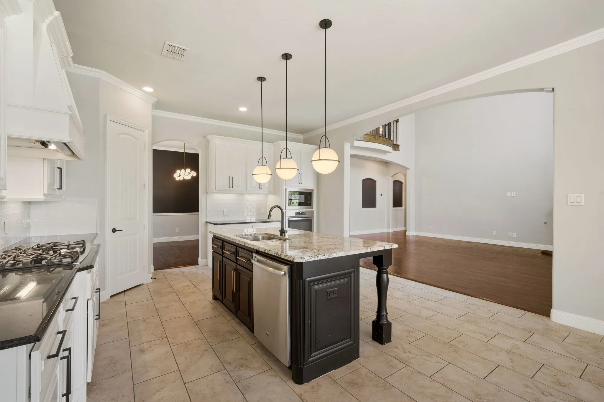 Chef's kitchen featuring a large center island with black cabinetry and white quartz countertops, stainless steel appliances including a gas cooktop and built-in refrigerator, pendant lighting, and neutral tile flooring throughout the open layout