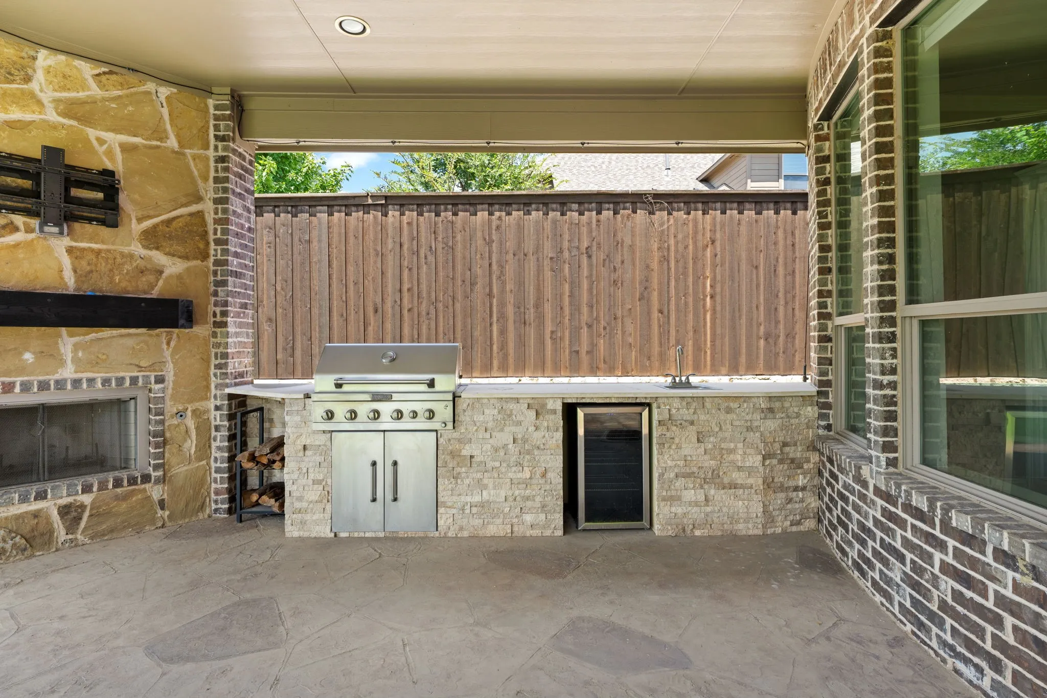 Covered patio with a stone fireplace, built-in stainless steel grill, beverage refrigerator, and stamped concrete flooring