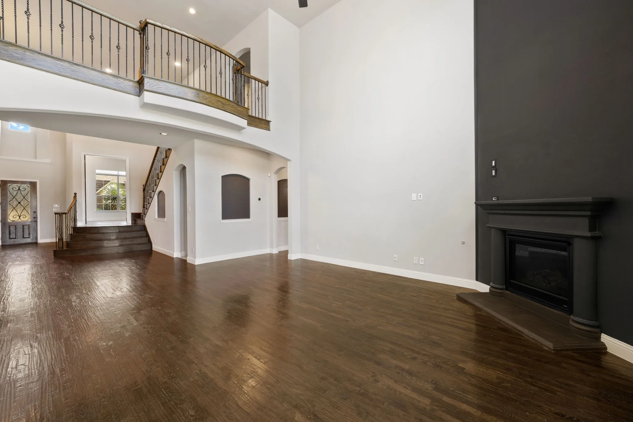 Vast open-concept space featuring wood-finish flooring, a decorative fireplace with mantel, and a multi-level staircase with wrought iron railing