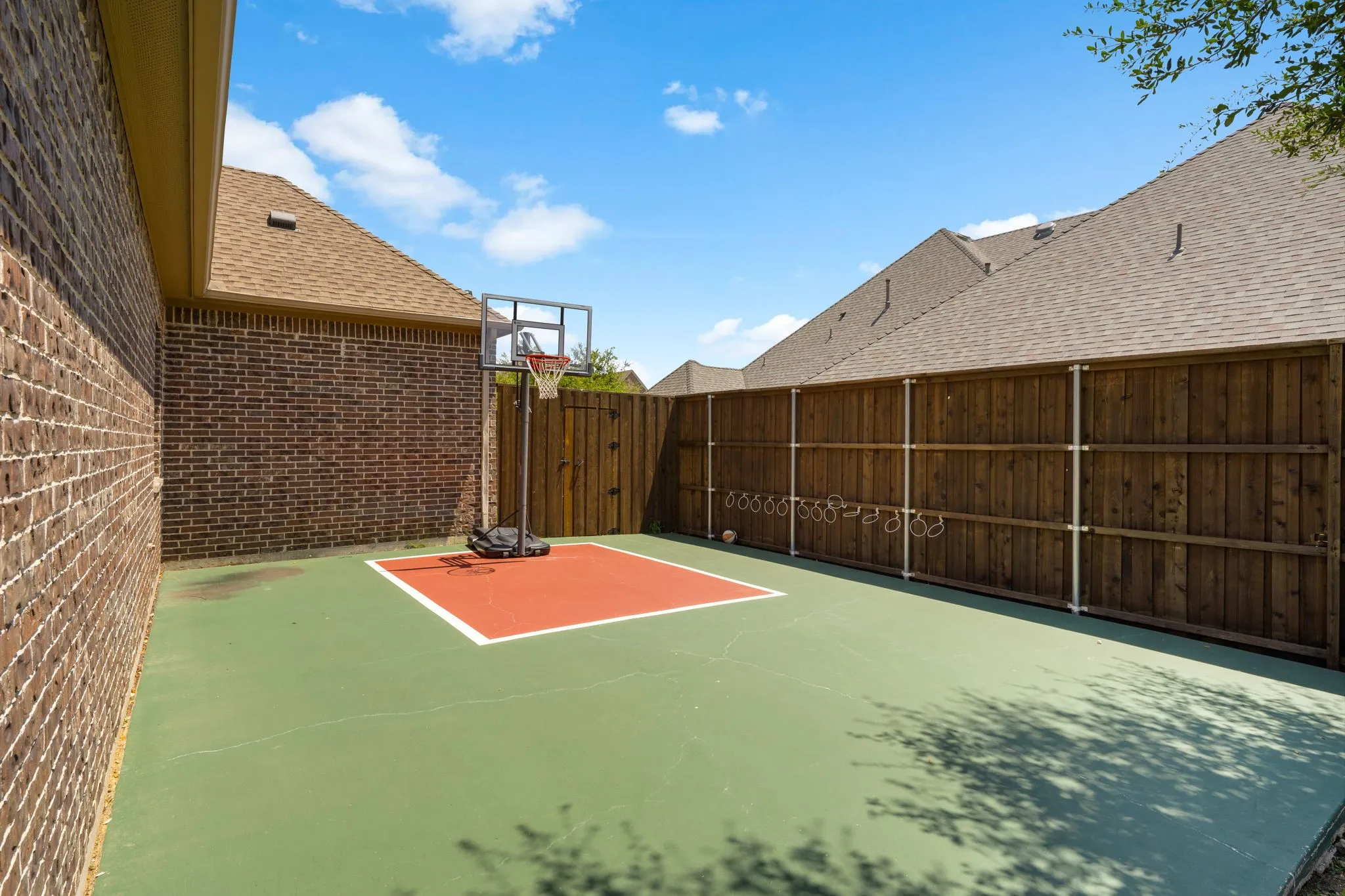 Outdoor court area with a green surface, a red-painted basketball key, and a privacy fence