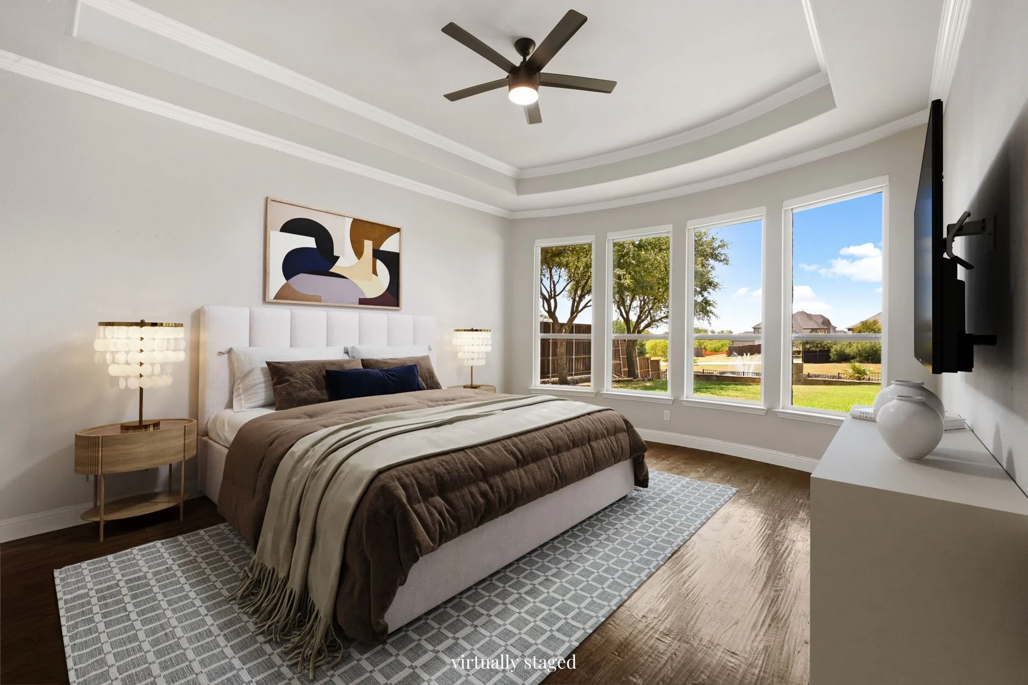 Recessed ceiling with layered crown molding, wood-finish flooring, and multiple large windows