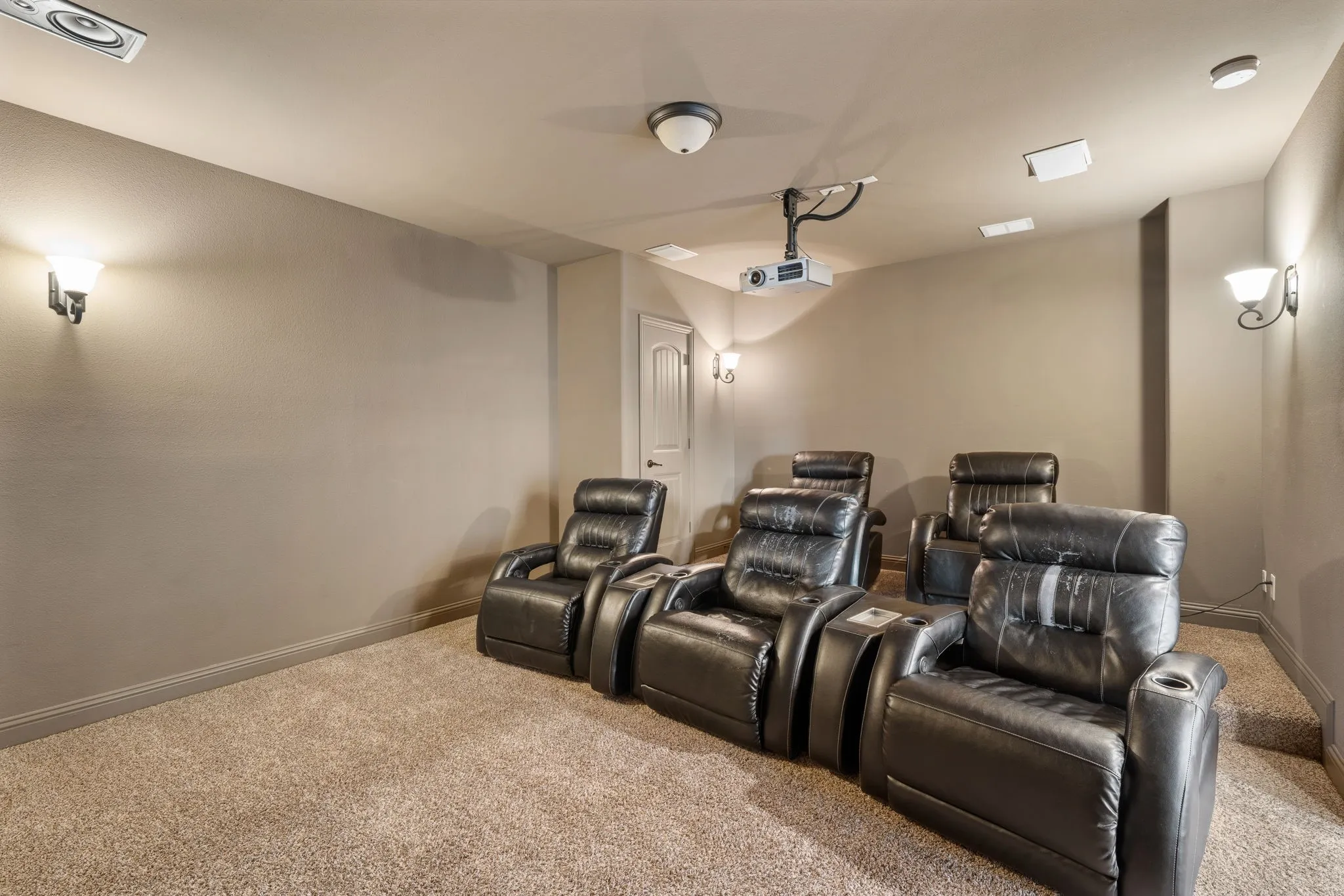 Integrated ceiling projector with mounted ceiling speakers, wall sconces, ceiling-mounted lighting, and carpeted flooring