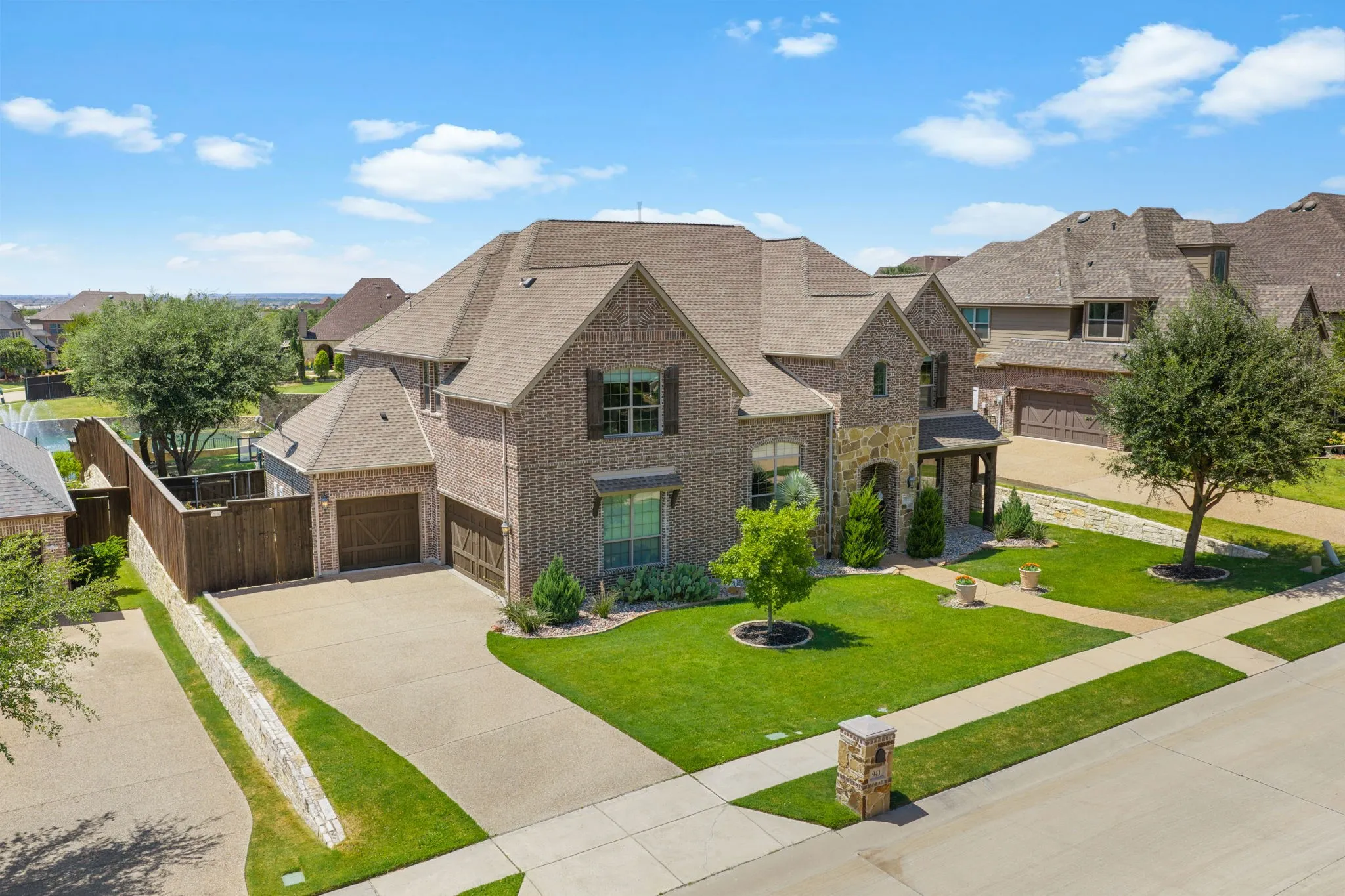 Brick exterior with stone accents, covered entry, attached multi-car garage, and established landscaping