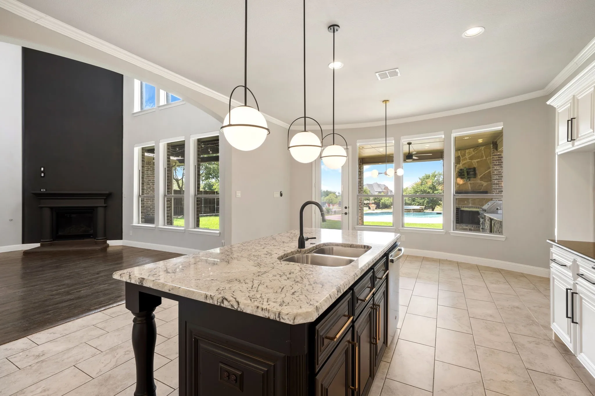Gourmet kitchen featuring a large center island with decorative turned legs, white cabinetry, quartz countertop, undermount sink with matte black faucet, pendant lighting, stainless steel appliances, and abundant natural light from expansive multi-pane windows overlooking manicured grounds