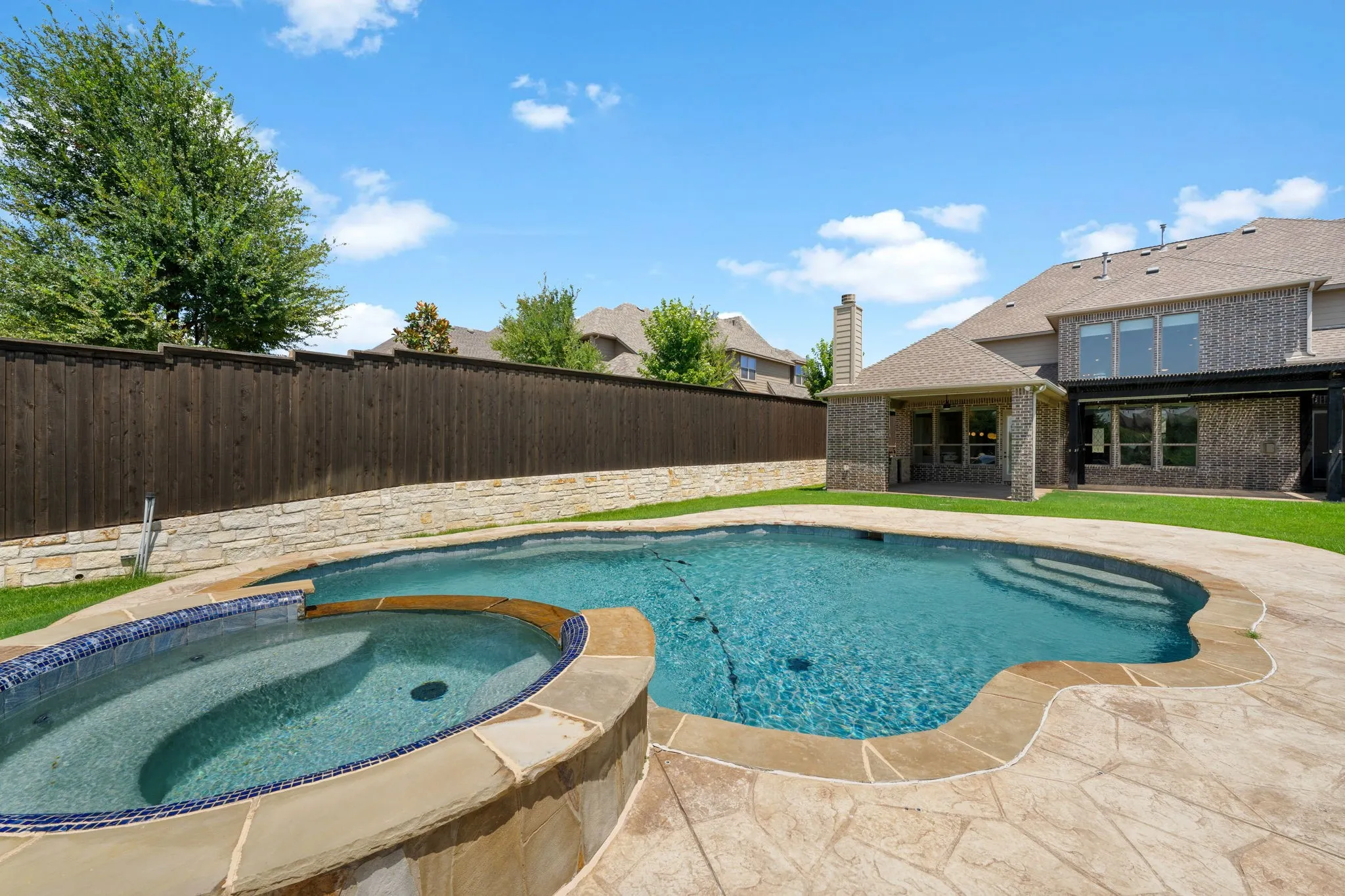 Sparkling resort-style backyard oasis featuring a lagoon-shaped saltwater pool with curved coping, adjoining spa with integrated jets, and expansive travertine decking