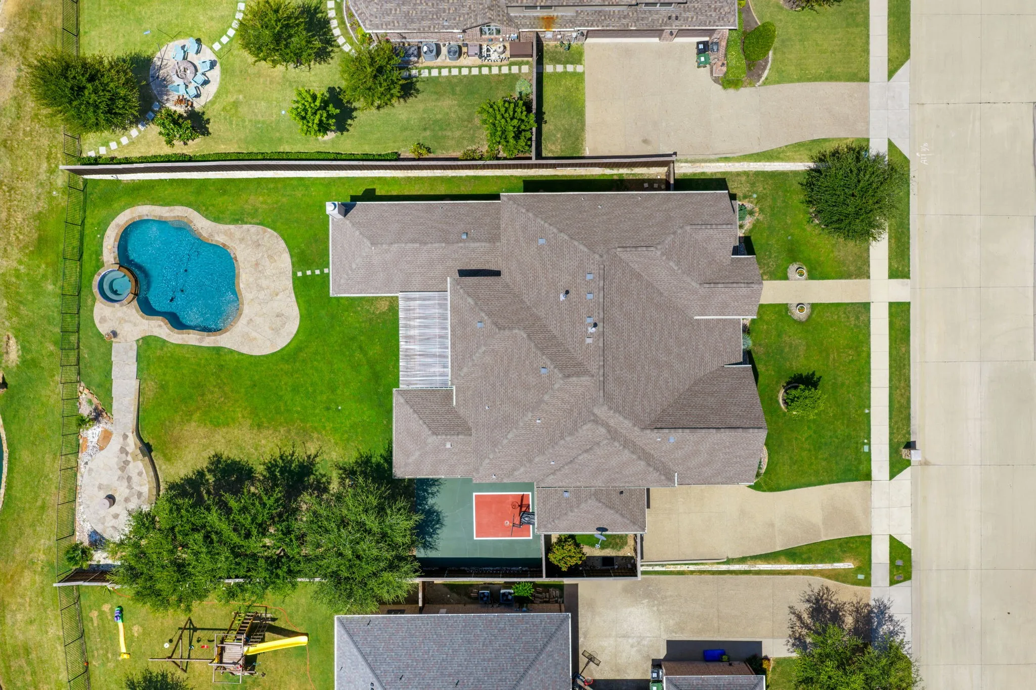 Curved swimming pool with an integrated spa, expansive green lawn, and a multi-sport court