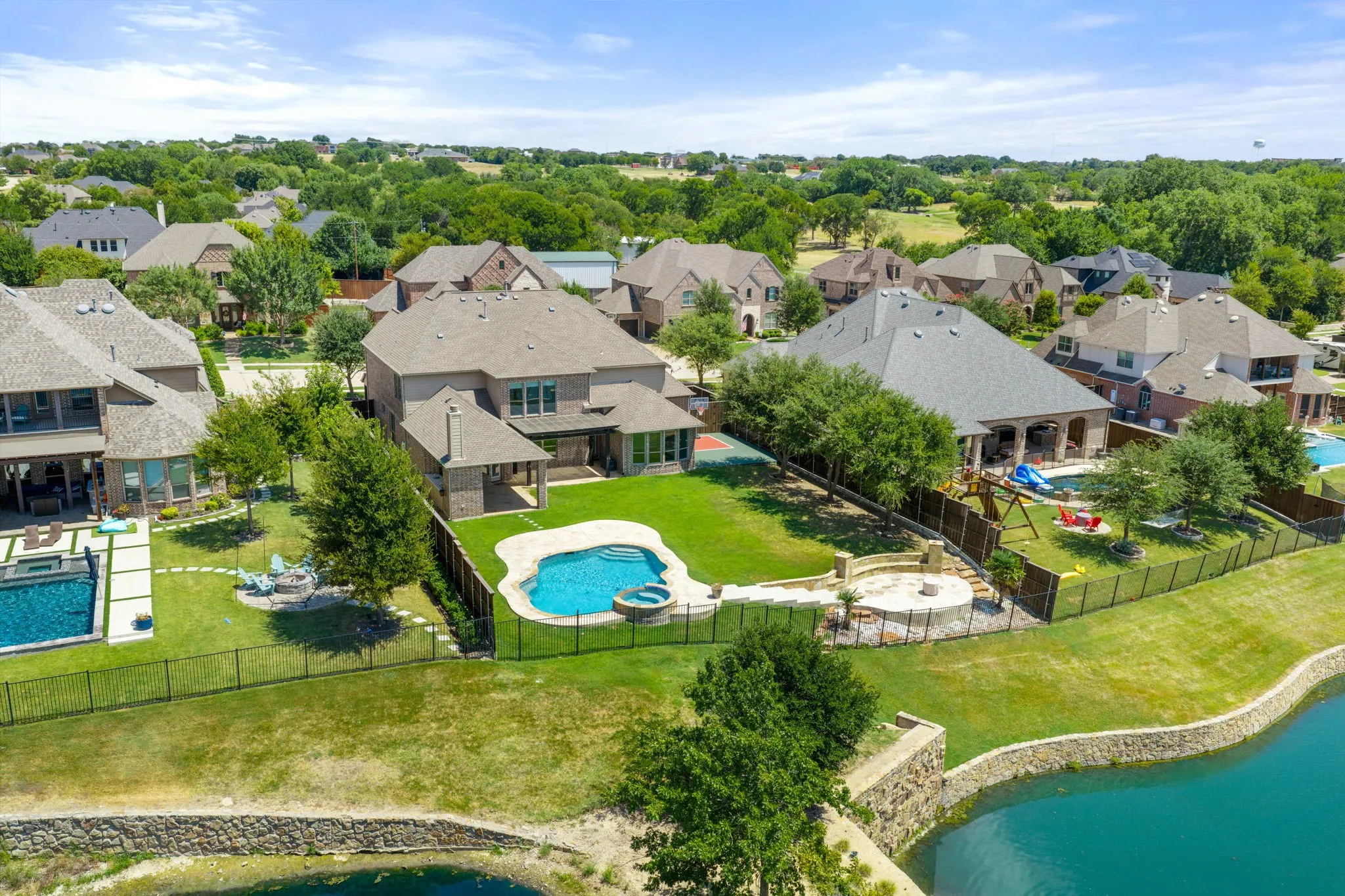 Expansive backyard featuring a manicured lawn, a freeform swimming pool with an integrated spa, and a stone-paved patio with a fire pit