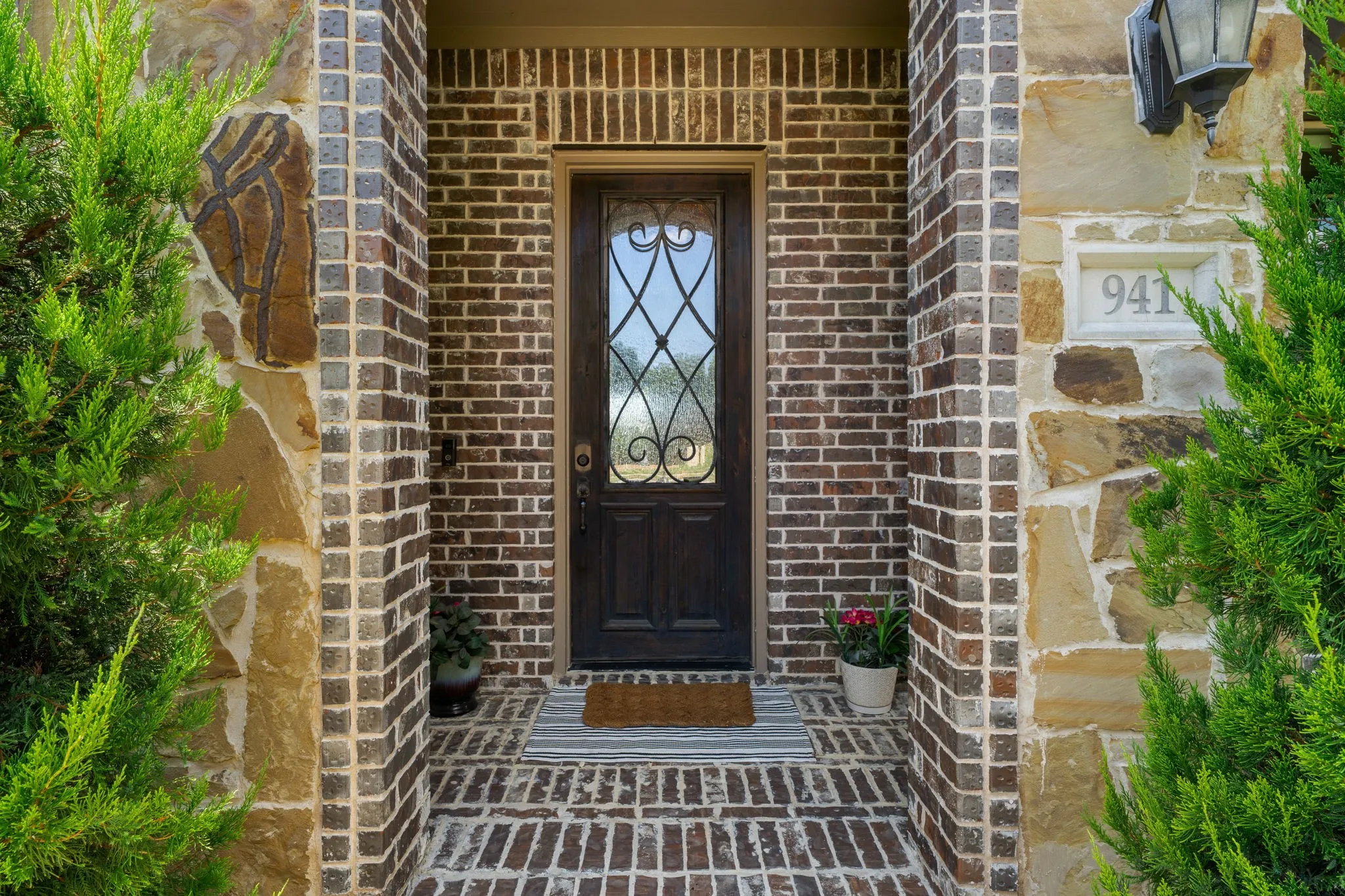 Brick and stone veneer exterior with a dark wood entry door featuring decorative ironwork and an overhead outdoor light fixture