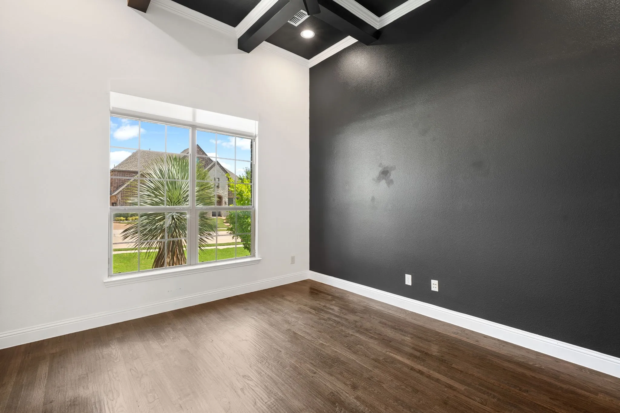 Modern oficefeaturing abundant natural light from a large multi-pane window, wood-finish flooring, a dramatic accent wall with matte black finish, recessed ceiling lighting, and white trim detailing