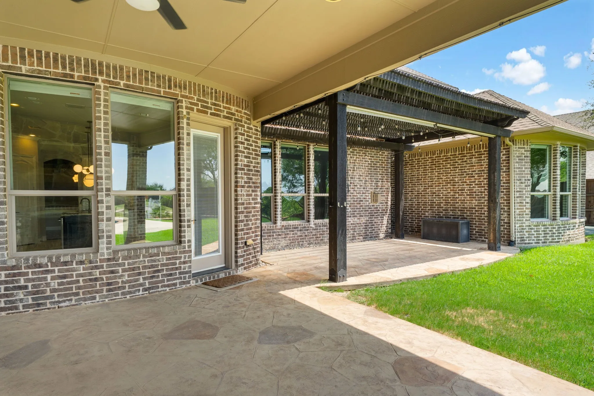 Covered patio with stamped concrete flooring, brick exterior, and a ceiling fan