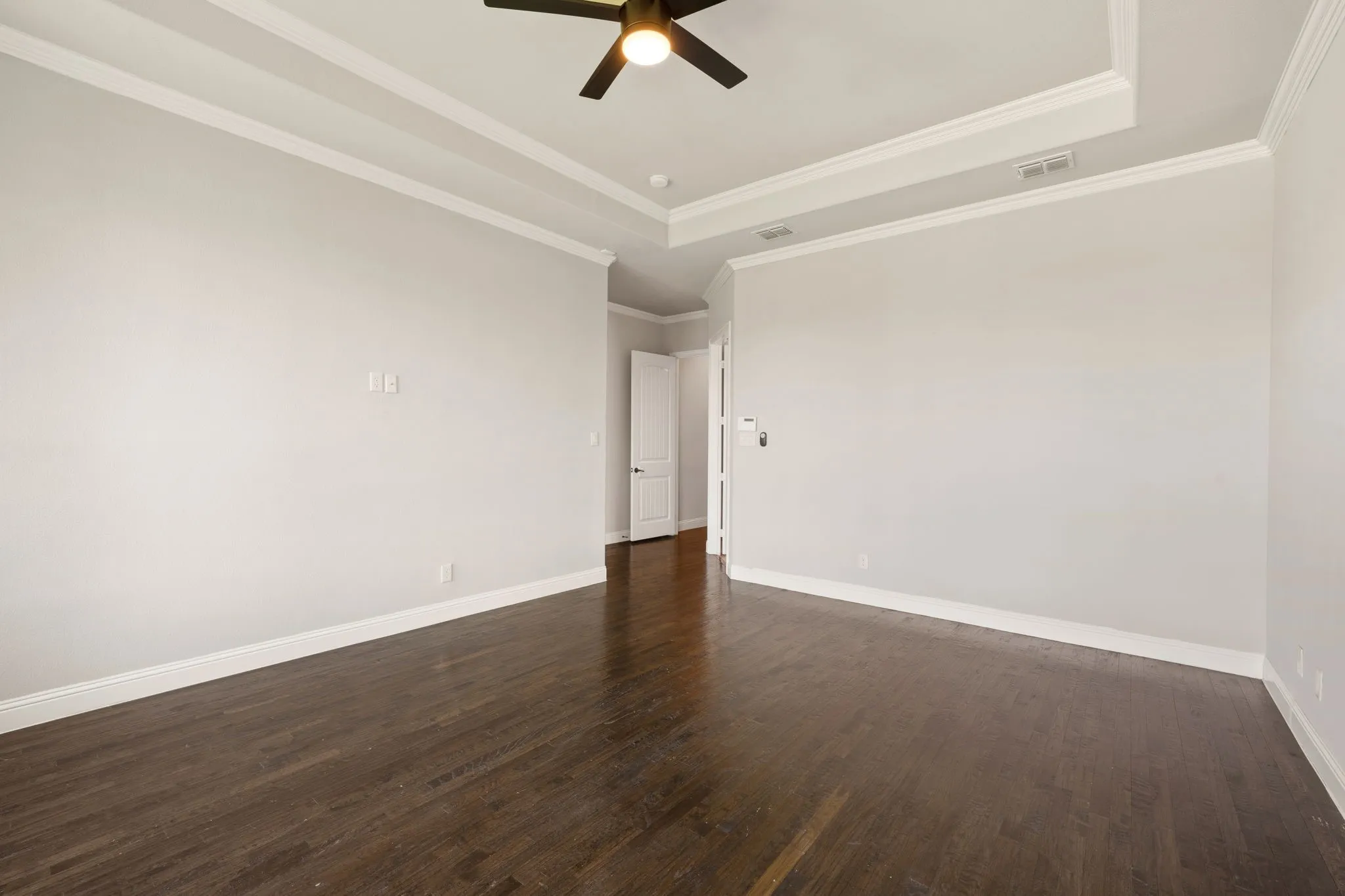 Spacious room featuring rich wood-finish flooring, white walls, and a coffered ceiling with recessed lighting and ceiling fan