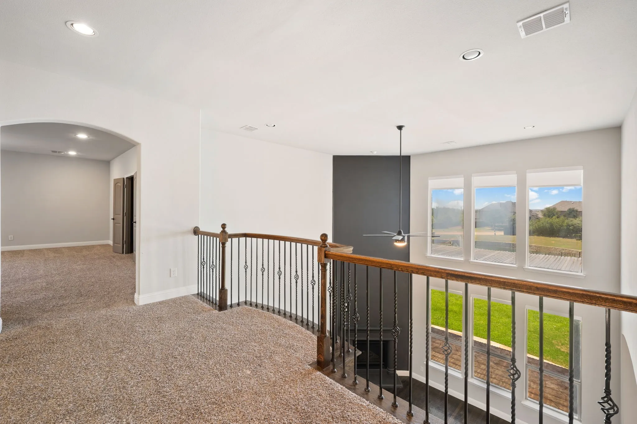 Carpeted loft area with recessed lighting, a ceiling fan, and a wrought iron and wood railing