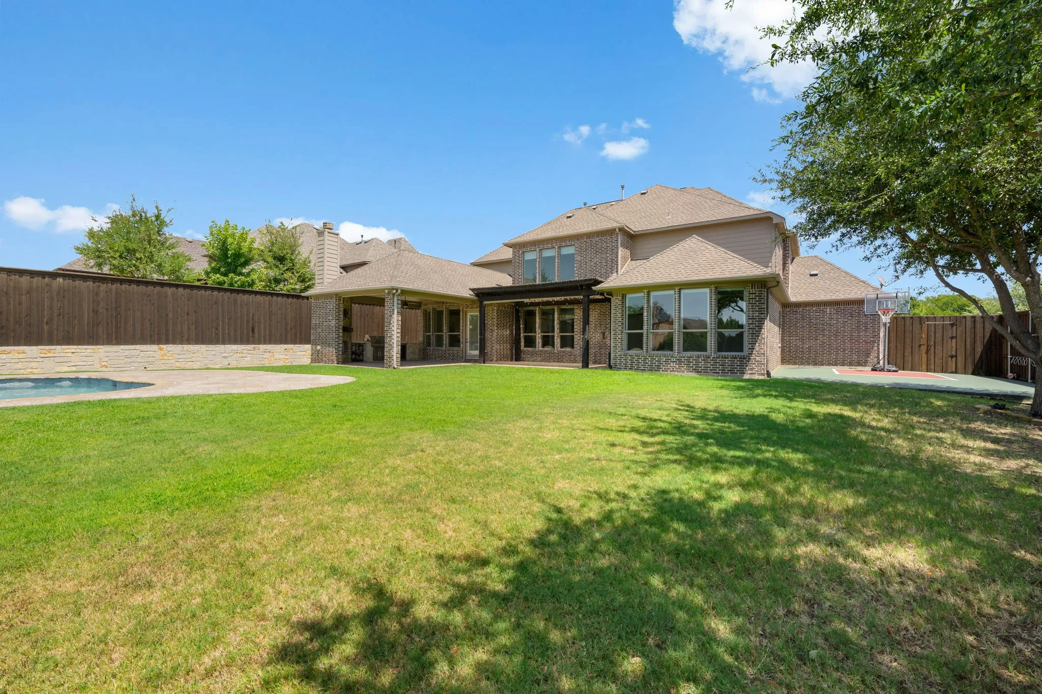 Expansive backyard featuring a manicured lawn, an in-ground pool with stone coping, and a covered patio with brick columns