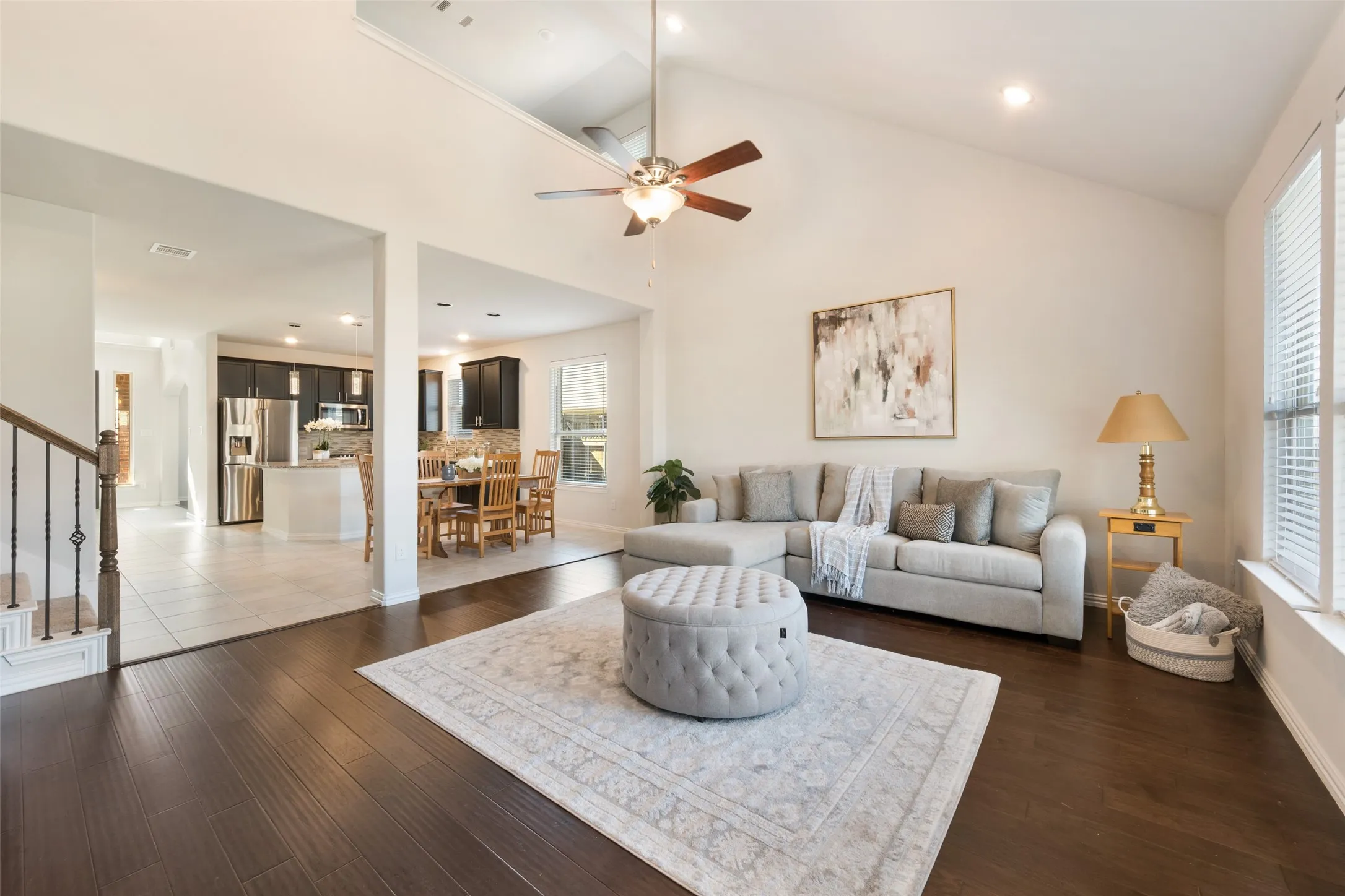 Open-concept living space featuring dark wood-finish flooring throughout, soaring ceilings with ceiling fan, and abundant natural light from multiple windows