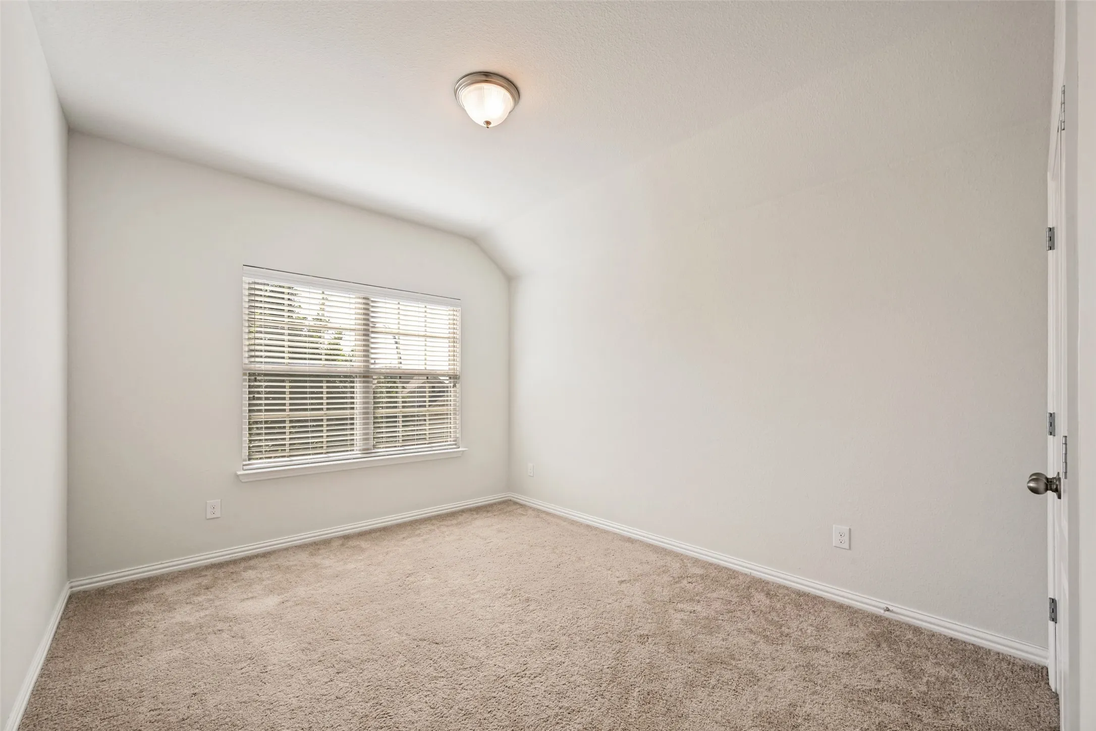 Neutral tone wall paint, vaulted ceiling, single window with blinds, carpet flooring, and flush mount lighting