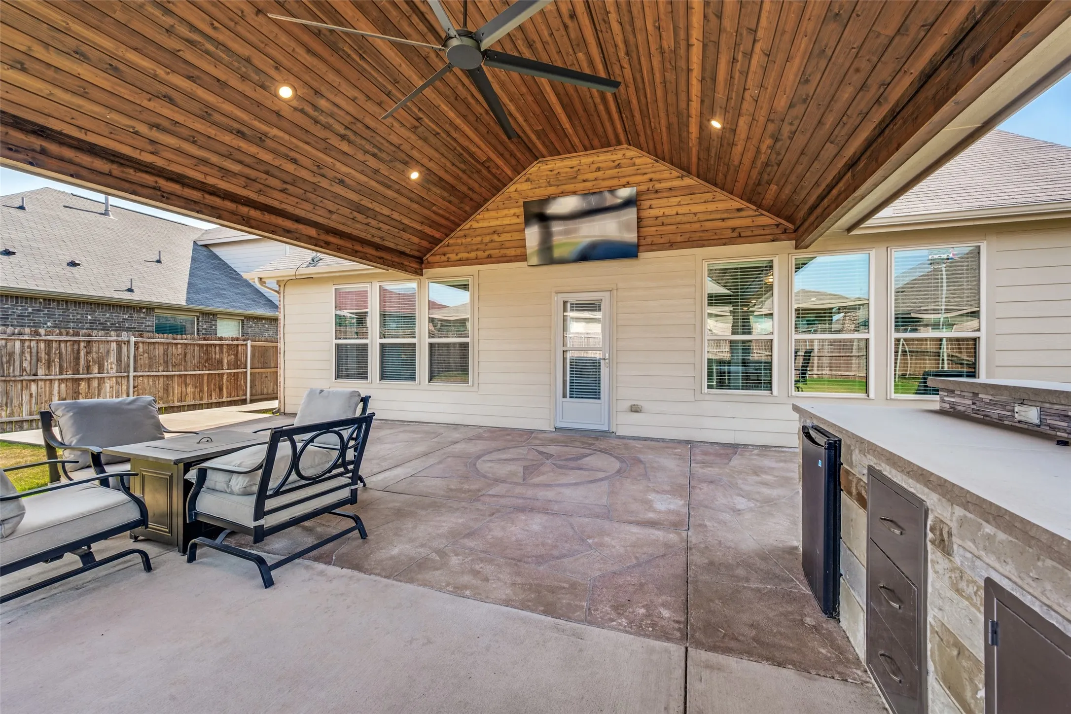 Expansive covered patio with wood-finish ceiling, recessed lighting, and ceiling fan overlooking a concrete entertaining space