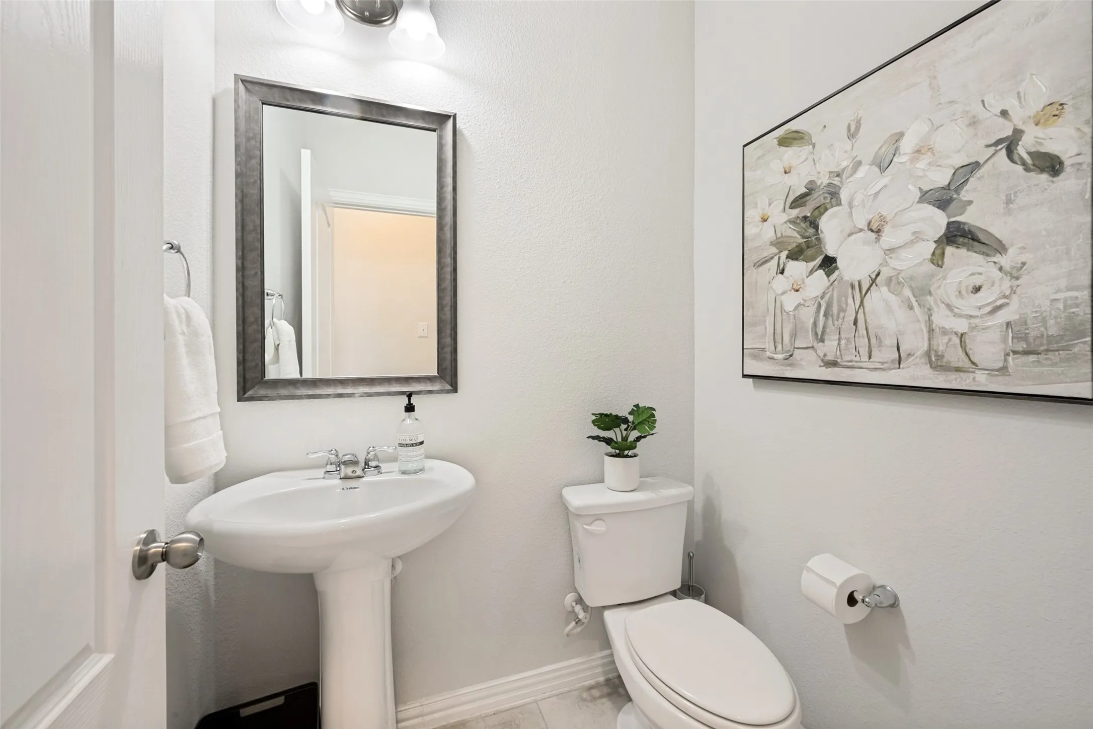 Pedestal sink with chrome faucet, framed mirror, and two-bulb vanity light fixture