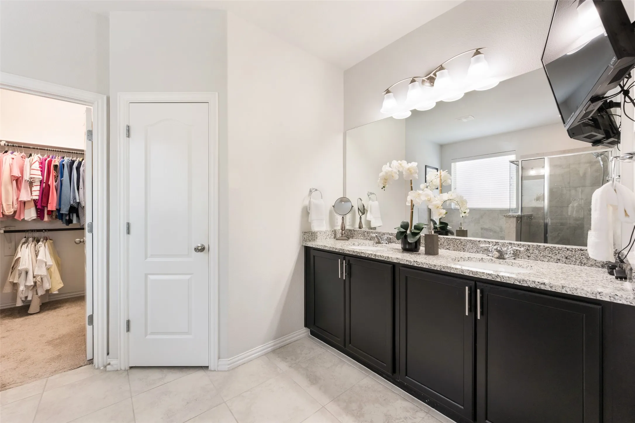 Spa-inspired primary bathroom featuring a black vanity with dual sinks, polished stone countertops, and chrome hardware