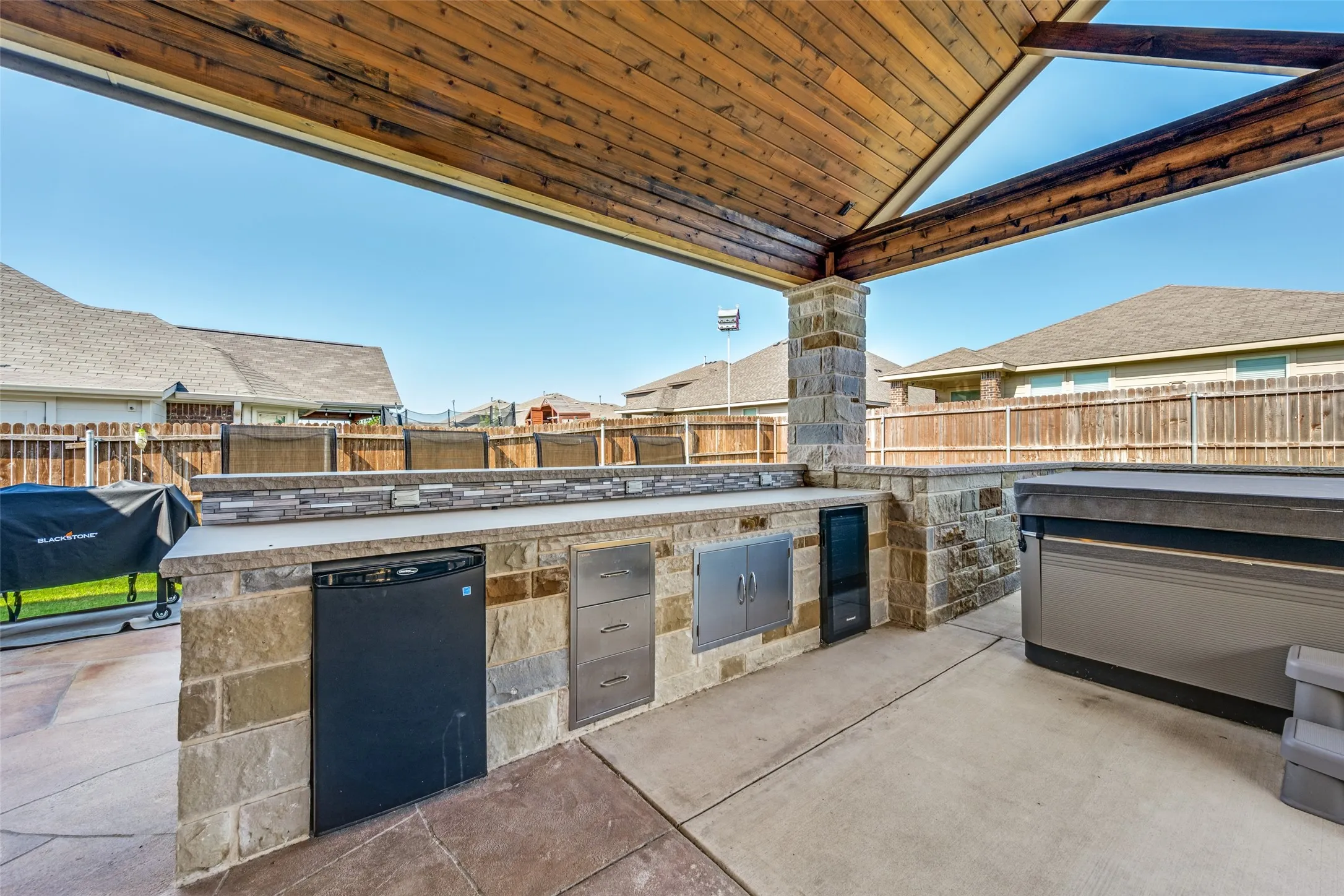 Covered outdoor kitchen featuring built-in cabinetry, refrigeration, stone-finish masonry, and a wood-beamed​​‌​​​​‌​​‌‌​‌‌​​​‌‌​‌​‌​‌​​​‌​​ ceiling