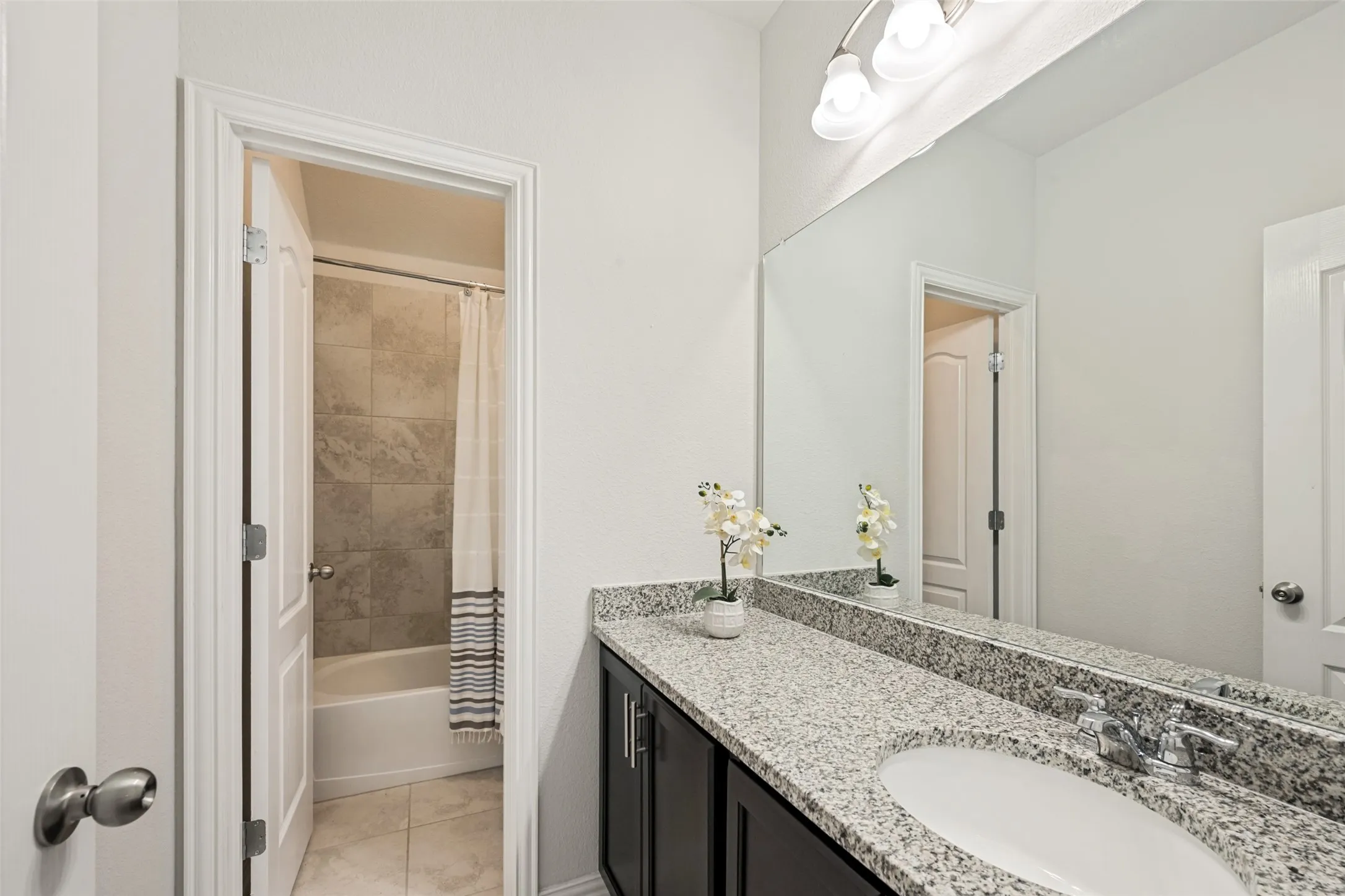 Spa-inspired master bathroom featuring a dual-sink vanity with speckled stone countertop, sleek matte black hardware, and an expansive framed mirror illuminated by overhead lighting