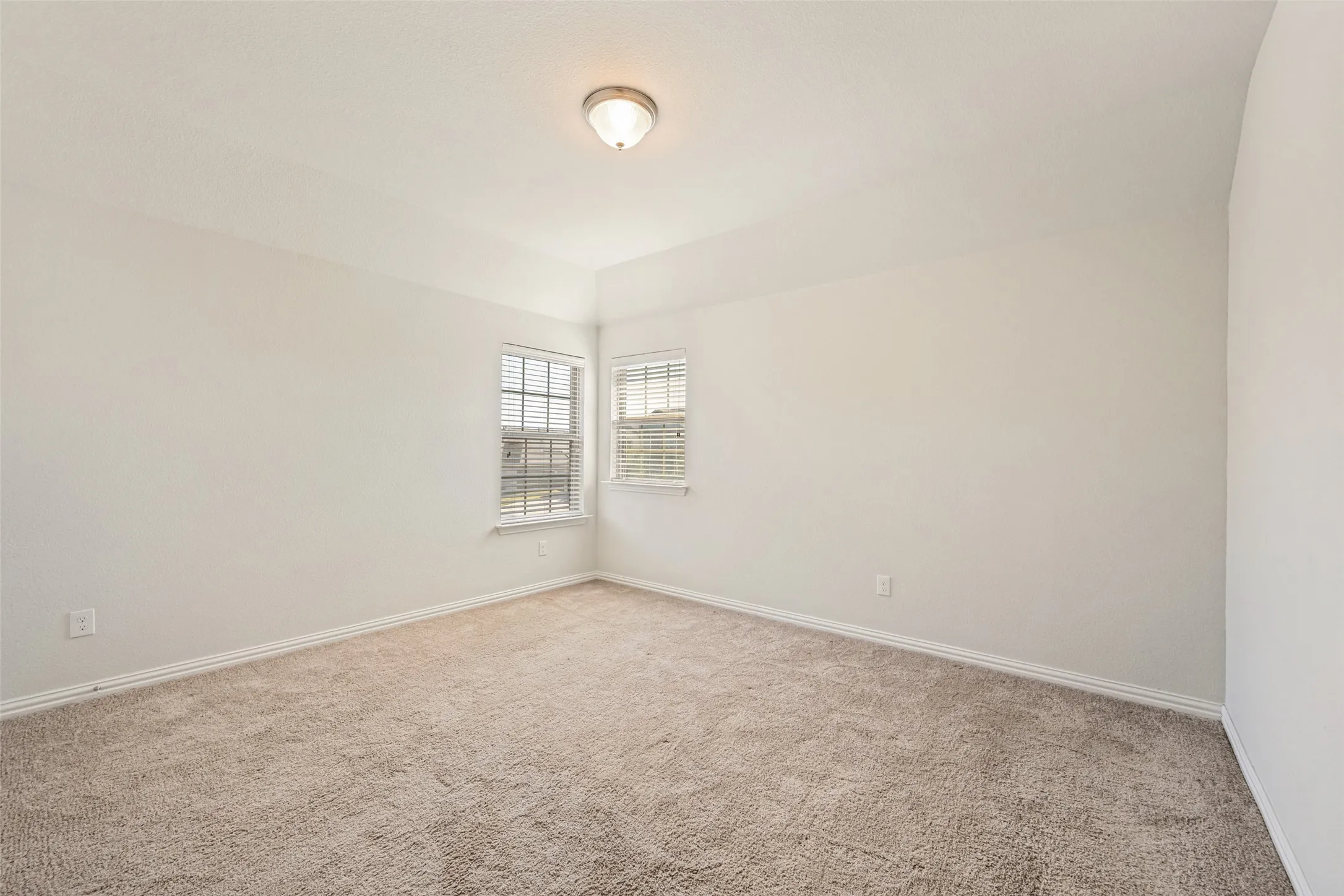 Bright corner bedroom with dual windows providing natural light, neutral carpet flooring, and fresh white wall finishes