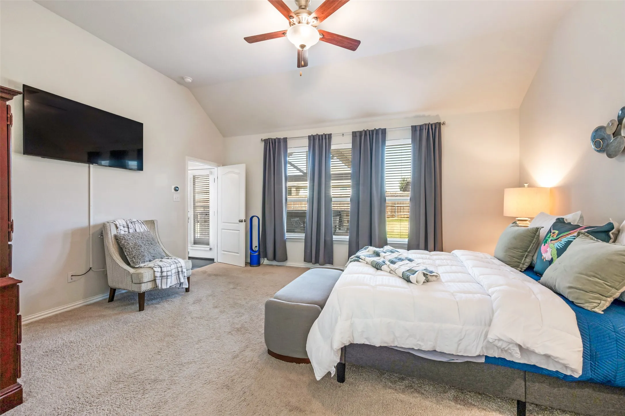 Spacious primary bedroom suite featuring vaulted ceilings, ceiling fan with integrated lighting, wall-mounted flat-screen television, and glass sliding doors opening to a private balcony