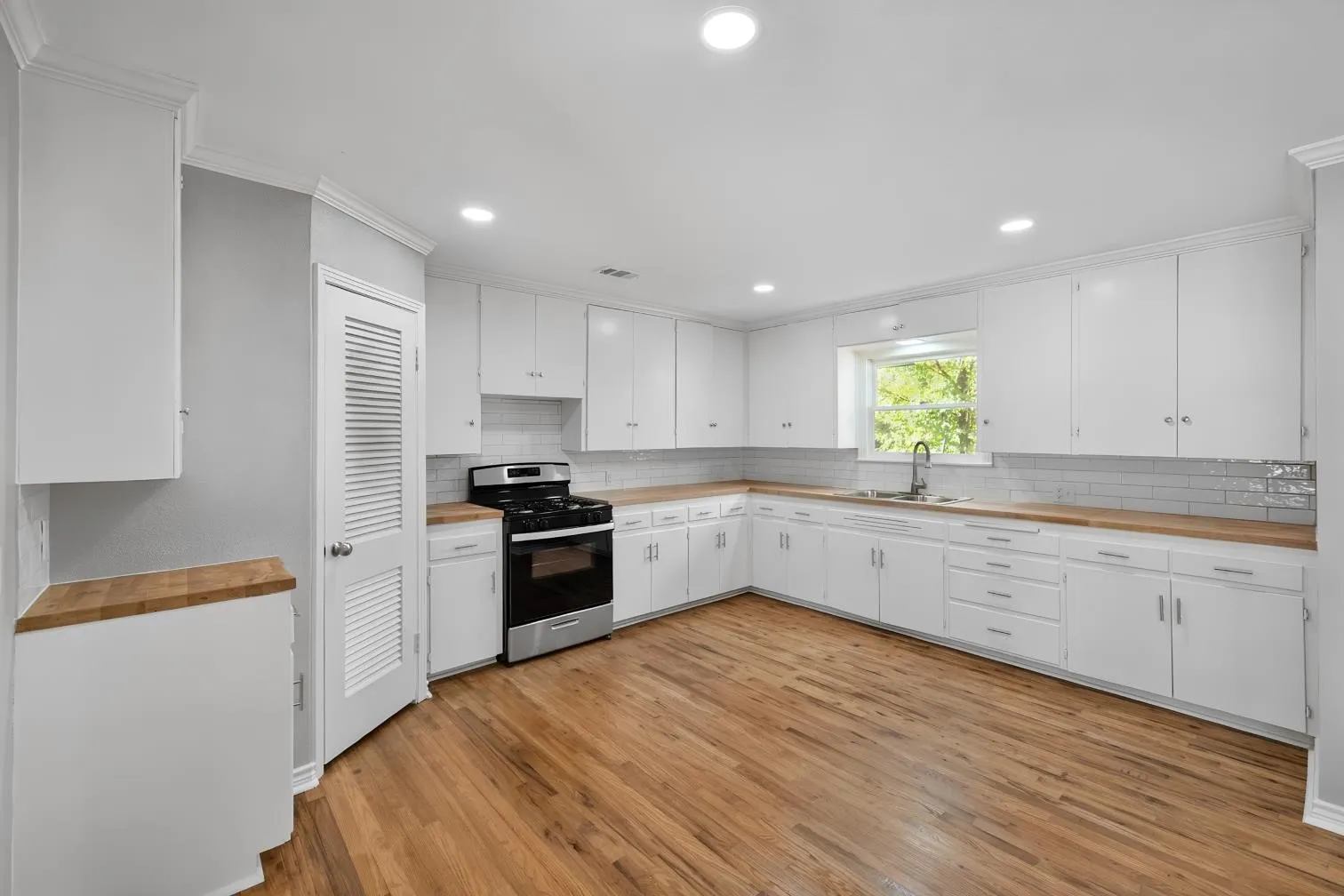 Kitchen featuring wood-finish flooring, white cabinetry, butcher block countertops, and a subway tile backsplash