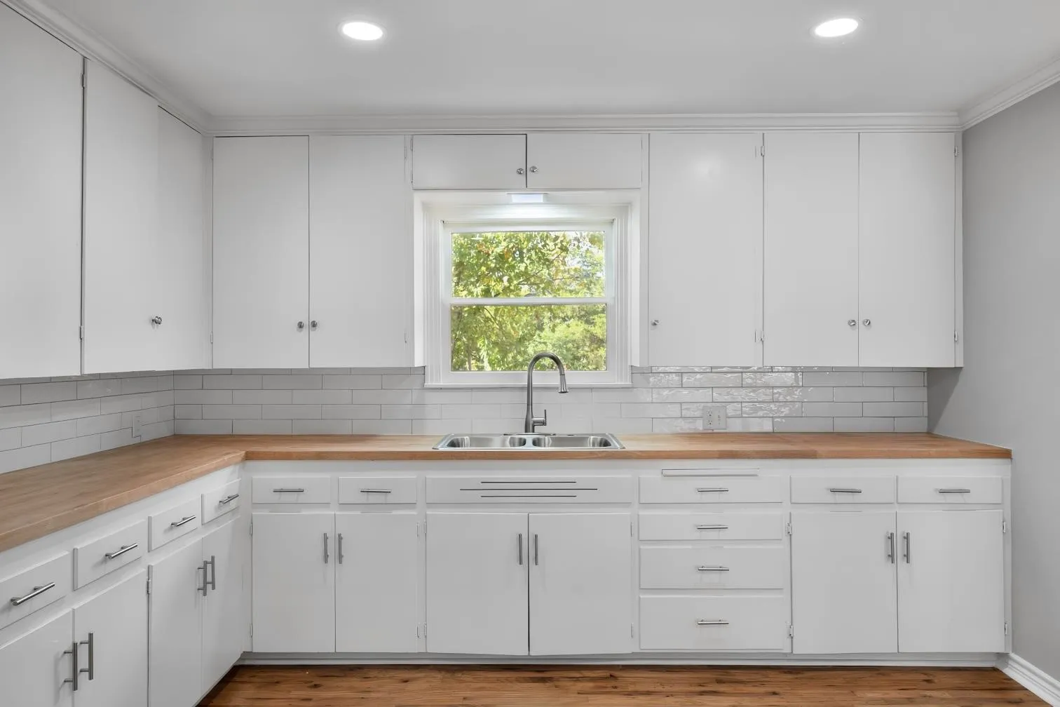 White cabinetry with silver hardware, butcher block countertops, subway tile backsplash, stainless steel sink, and wood-finish flooring